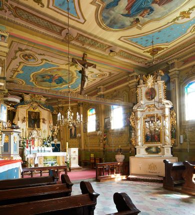 Zdjęcie nr 16: Polichromia ścian kościoła odpowiada podziałom architektonicznym wnętrza wydzielonym przez pilastry. Malowany zielony cokół w jednej czwartej wysokości ścian wyodrębniony jest pasem ornamentu geometrycznego, w nawie w jego polu znajdują się żółte prostokąty z dekoracją geometryczną, w prezbiterium malowana jasnozielona tkanina z dwoma pasami ornamentu roślinnego, medalionami z monogramami Marii i koronami oraz z motywem lilii heraldycznych i rozet. Trzony pilastrów wnętrza bladożółte z malowanymi płycinami dekorowanymi kampanulami, głowice zdobione malowanym kimationem. Na osi pilastrów, w partii fryzu, na tle niebieskich prostokątów uskrzydlone główki anielskie, pomiędzy nimi fryz wypełniony różowo-pomarańczowymi malowanymi płycinami w błękitnym obramieniu o fantazyjnym wykroju, dekorowanymi kampanulami. Belkowanie zamknięte malowanym pasem ornamentu geometrycznego. W polach pomiędzy pilastrami malowane płyciny o fantazyjnym kształcie zbliżonym do prostokąta, ujęte ramą zakończoną kartuszem, ich pola wypełnione są dekoracją geometryczną składającą się z krzyży równoramiennych w glorii i rozet wykonanych techniką patronową. Otwory okienne ujęte są malowanymi, imitującymi profilowanie obramieniami, otwory drzwiowe iluzjonistycznymi portalami z uszakami: portal w nawie zwieńczony jest kartuszem, a portal w prezbiterium zwieńczony jest szczytem zamkniętym fragmentem gzymsu w formie łuku segmentowego nadwieszonego podtrzymywanym przez spływy wolutowe. Pod chórem muzycznym malowane tablice pamiątkowe ujęte ramą, na ścianie północnej z napisem: „Ecclam hanc sub titulo Assumptionis B.V. Mariae a strenuo / milite Wierzbięta in Branice et Ruszcza Haerede pimo in / Wola juxta fines villae Stryjów a D. 1386 fundatam decimis / ex praedio Branice a colonis Stryjów, Wola, cuius sors est Grabie / Szczurów Zymbrzeg et ibidem taberna cum duobus pratis ac lacubus / Orzek et Piotrek ditatam, proper alluviem Vistulae  curatus suus / in hunc locum, qui erat pratum Gruczyn, ecclae dotale transtulit, / Hac tandem post annos 356 collapsa, quam vides, A.R.D. Jacobus Cichoński, parochus Grabiensis a.D. 1742 in loco desolatae  novam erexit. / Consecravit Illmus ac Rmus Michaël Kunicki, Sufraganeus Eppus. / Cracoviensis, Abbas Clarae Tumbae a D. 1749. / Restauravit A.R.D. Josephus Raźny, parochus Grabiensis a.D. 1907. / e colectis parochianorum.”; na ścianie południowej z napisem: „Ku Pamięci! / Dzieci Moje Najmilsze - Ja Prastara Świątynia / Polska dziękuję Wam za serdeczną troskę / o mnie. Oto dzięki Waszym ofiarom Drodzy / Rodzice i Twoim wysiłkom Kochana Młodzieży / w r. 1959 odnowiło się moje oblicze - rozjaśniały /  moje ołtarze, a w r. 1960 zabrzmiał mój nowy / organ na większą chwałę Bożą. Ja Was za to / rodzę na nowo do życia łaski. Ja Was błogosławię / na życie rodzinne. Ja Was prowadzę ku Bogu. Ja / Was także żegnam poraz ostatni, gdy przechodzicie / z tego padołu płaczu do wieczności, aby / Was znowu powitać kiedyś w niebie.”. Na ścianie zachodniej, pod chórem, nad środkowym otworem przejściowym pozostałości dawnego iluzjonistycznego portalu z kartuszem herbowym. Na stropie prezbiterium wydzielone pole o kształcie powtarzającym plan prezbiterium, wewnątrz pole w formie kwadratu o wklęsłych narożach z wpisanym polem o fantazyjnym zarysie zbliżonym do owalu ze sceną Wniebowzięcia Najświętszej Marii Panny. W narożach owalne pola z czterema istotami apokaliptycznymi. Prosta belka tęczowa w kolorze zielonym, o profilowaniach w kolorze niebieskim i różowym, z napisem: „JEZU ZMIŁUJ SIĘ NAD NAMI”. Na stropie nawy prostokątne pole wydzielone grubym bladoróżowym obramieniem z płycinami o nieregularnym kształcie wypełnionymi kratką regencyjną i rozetami alternowanymi medalionami z rozetami, naroża dekorowane są wstęgą regencyjną i akantem. Wewnątrz pole o fantazyjnym wykroju zbliżonym do owalu ze sceną Koronacji Najświętszej Marii Panny, flankowane przez dwie malowane błękitne płyciny o nieregularnym kształcie wypełnione rozetkami. W narożach, w ozdobnych kartuszach herby Pogoni Litewskiej i Orła Białego.
