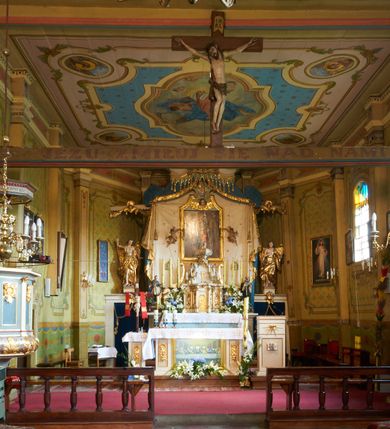 Zdjęcie nr 13: Polichromia ścian kościoła odpowiada podziałom architektonicznym wnętrza wydzielonym przez pilastry. Malowany zielony cokół w jednej czwartej wysokości ścian wyodrębniony jest pasem ornamentu geometrycznego, w nawie w jego polu znajdują się żółte prostokąty z dekoracją geometryczną, w prezbiterium malowana jasnozielona tkanina z dwoma pasami ornamentu roślinnego, medalionami z monogramami Marii i koronami oraz z motywem lilii heraldycznych i rozet. Trzony pilastrów wnętrza bladożółte z malowanymi płycinami dekorowanymi kampanulami, głowice zdobione malowanym kimationem. Na osi pilastrów, w partii fryzu, na tle niebieskich prostokątów uskrzydlone główki anielskie, pomiędzy nimi fryz wypełniony różowo-pomarańczowymi malowanymi płycinami w błękitnym obramieniu o fantazyjnym wykroju, dekorowanymi kampanulami. Belkowanie zamknięte malowanym pasem ornamentu geometrycznego. W polach pomiędzy pilastrami malowane płyciny o fantazyjnym kształcie zbliżonym do prostokąta, ujęte ramą zakończoną kartuszem, ich pola wypełnione są dekoracją geometryczną składającą się z krzyży równoramiennych w glorii i rozet wykonanych techniką patronową. Otwory okienne ujęte są malowanymi, imitującymi profilowanie obramieniami, otwory drzwiowe iluzjonistycznymi portalami z uszakami: portal w nawie zwieńczony jest kartuszem, a portal w prezbiterium zwieńczony jest szczytem zamkniętym fragmentem gzymsu w formie łuku segmentowego nadwieszonego podtrzymywanym przez spływy wolutowe. Pod chórem muzycznym malowane tablice pamiątkowe ujęte ramą, na ścianie północnej z napisem: „Ecclam hanc sub titulo Assumptionis B.V. Mariae a strenuo / milite Wierzbięta in Branice et Ruszcza Haerede pimo in / Wola juxta fines villae Stryjów a D. 1386 fundatam decimis / ex praedio Branice a colonis Stryjów, Wola, cuius sors est Grabie / Szczurów Zymbrzeg et ibidem taberna cum duobus pratis ac lacubus / Orzek et Piotrek ditatam, proper alluviem Vistulae  curatus suus / in hunc locum, qui erat pratum Gruczyn, ecclae dotale transtulit, / Hac tandem post annos 356 collapsa, quam vides, A.R.D. Jacobus Cichoński, parochus Grabiensis a.D. 1742 in loco desolatae  novam erexit. / Consecravit Illmus ac Rmus Michaël Kunicki, Sufraganeus Eppus. / Cracoviensis, Abbas Clarae Tumbae a D. 1749. / Restauravit A.R.D. Josephus Raźny, parochus Grabiensis a.D. 1907. / e colectis parochianorum.”; na ścianie południowej z napisem: „Ku Pamięci! / Dzieci Moje Najmilsze - Ja Prastara Świątynia / Polska dziękuję Wam za serdeczną troskę / o mnie. Oto dzięki Waszym ofiarom Drodzy / Rodzice i Twoim wysiłkom Kochana Młodzieży / w r. 1959 odnowiło się moje oblicze - rozjaśniały /  moje ołtarze, a w r. 1960 zabrzmiał mój nowy / organ na większą chwałę Bożą. Ja Was za to / rodzę na nowo do życia łaski. Ja Was błogosławię / na życie rodzinne. Ja Was prowadzę ku Bogu. Ja / Was także żegnam poraz ostatni, gdy przechodzicie / z tego padołu płaczu do wieczności, aby / Was znowu powitać kiedyś w niebie.”. Na ścianie zachodniej, pod chórem, nad środkowym otworem przejściowym pozostałości dawnego iluzjonistycznego portalu z kartuszem herbowym. Na stropie prezbiterium wydzielone pole o kształcie powtarzającym plan prezbiterium, wewnątrz pole w formie kwadratu o wklęsłych narożach z wpisanym polem o fantazyjnym zarysie zbliżonym do owalu ze sceną Wniebowzięcia Najświętszej Marii Panny. W narożach owalne pola z czterema istotami apokaliptycznymi. Prosta belka tęczowa w kolorze zielonym, o profilowaniach w kolorze niebieskim i różowym, z napisem: „JEZU ZMIŁUJ SIĘ NAD NAMI”. Na stropie nawy prostokątne pole wydzielone grubym bladoróżowym obramieniem z płycinami o nieregularnym kształcie wypełnionymi kratką regencyjną i rozetami alternowanymi medalionami z rozetami, naroża dekorowane są wstęgą regencyjną i akantem. Wewnątrz pole o fantazyjnym wykroju zbliżonym do owalu ze sceną Koronacji Najświętszej Marii Panny, flankowane przez dwie malowane błękitne płyciny o nieregularnym kształcie wypełnione rozetkami. W narożach, w ozdobnych kartuszach herby Pogoni Litewskiej i Orła Białego.
