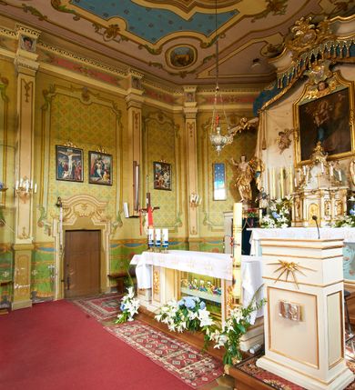 Zdjęcie nr 17: Polichromia ścian kościoła odpowiada podziałom architektonicznym wnętrza wydzielonym przez pilastry. Malowany zielony cokół w jednej czwartej wysokości ścian wyodrębniony jest pasem ornamentu geometrycznego, w nawie w jego polu znajdują się żółte prostokąty z dekoracją geometryczną, w prezbiterium malowana jasnozielona tkanina z dwoma pasami ornamentu roślinnego, medalionami z monogramami Marii i koronami oraz z motywem lilii heraldycznych i rozet. Trzony pilastrów wnętrza bladożółte z malowanymi płycinami dekorowanymi kampanulami, głowice zdobione malowanym kimationem. Na osi pilastrów, w partii fryzu, na tle niebieskich prostokątów uskrzydlone główki anielskie, pomiędzy nimi fryz wypełniony różowo-pomarańczowymi malowanymi płycinami w błękitnym obramieniu o fantazyjnym wykroju, dekorowanymi kampanulami. Belkowanie zamknięte malowanym pasem ornamentu geometrycznego. W polach pomiędzy pilastrami malowane płyciny o fantazyjnym kształcie zbliżonym do prostokąta, ujęte ramą zakończoną kartuszem, ich pola wypełnione są dekoracją geometryczną składającą się z krzyży równoramiennych w glorii i rozet wykonanych techniką patronową. Otwory okienne ujęte są malowanymi, imitującymi profilowanie obramieniami, otwory drzwiowe iluzjonistycznymi portalami z uszakami: portal w nawie zwieńczony jest kartuszem, a portal w prezbiterium zwieńczony jest szczytem zamkniętym fragmentem gzymsu w formie łuku segmentowego nadwieszonego podtrzymywanym przez spływy wolutowe. Pod chórem muzycznym malowane tablice pamiątkowe ujęte ramą, na ścianie północnej z napisem: „Ecclam hanc sub titulo Assumptionis B.V. Mariae a strenuo / milite Wierzbięta in Branice et Ruszcza Haerede pimo in / Wola juxta fines villae Stryjów a D. 1386 fundatam decimis / ex praedio Branice a colonis Stryjów, Wola, cuius sors est Grabie / Szczurów Zymbrzeg et ibidem taberna cum duobus pratis ac lacubus / Orzek et Piotrek ditatam, proper alluviem Vistulae  curatus suus / in hunc locum, qui erat pratum Gruczyn, ecclae dotale transtulit, / Hac tandem post annos 356 collapsa, quam vides, A.R.D. Jacobus Cichoński, parochus Grabiensis a.D. 1742 in loco desolatae  novam erexit. / Consecravit Illmus ac Rmus Michaël Kunicki, Sufraganeus Eppus. / Cracoviensis, Abbas Clarae Tumbae a D. 1749. / Restauravit A.R.D. Josephus Raźny, parochus Grabiensis a.D. 1907. / e colectis parochianorum.”; na ścianie południowej z napisem: „Ku Pamięci! / Dzieci Moje Najmilsze - Ja Prastara Świątynia / Polska dziękuję Wam za serdeczną troskę / o mnie. Oto dzięki Waszym ofiarom Drodzy / Rodzice i Twoim wysiłkom Kochana Młodzieży / w r. 1959 odnowiło się moje oblicze - rozjaśniały /  moje ołtarze, a w r. 1960 zabrzmiał mój nowy / organ na większą chwałę Bożą. Ja Was za to / rodzę na nowo do życia łaski. Ja Was błogosławię / na życie rodzinne. Ja Was prowadzę ku Bogu. Ja / Was także żegnam poraz ostatni, gdy przechodzicie / z tego padołu płaczu do wieczności, aby / Was znowu powitać kiedyś w niebie.”. Na ścianie zachodniej, pod chórem, nad środkowym otworem przejściowym pozostałości dawnego iluzjonistycznego portalu z kartuszem herbowym. Na stropie prezbiterium wydzielone pole o kształcie powtarzającym plan prezbiterium, wewnątrz pole w formie kwadratu o wklęsłych narożach z wpisanym polem o fantazyjnym zarysie zbliżonym do owalu ze sceną Wniebowzięcia Najświętszej Marii Panny. W narożach owalne pola z czterema istotami apokaliptycznymi. Prosta belka tęczowa w kolorze zielonym, o profilowaniach w kolorze niebieskim i różowym, z napisem: „JEZU ZMIŁUJ SIĘ NAD NAMI”. Na stropie nawy prostokątne pole wydzielone grubym bladoróżowym obramieniem z płycinami o nieregularnym kształcie wypełnionymi kratką regencyjną i rozetami alternowanymi medalionami z rozetami, naroża dekorowane są wstęgą regencyjną i akantem. Wewnątrz pole o fantazyjnym wykroju zbliżonym do owalu ze sceną Koronacji Najświętszej Marii Panny, flankowane przez dwie malowane błękitne płyciny o nieregularnym kształcie wypełnione rozetkami. W narożach, w ozdobnych kartuszach herby Pogoni Litewskiej i Orła Białego.
