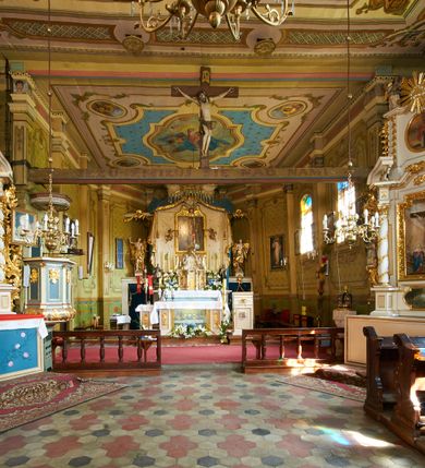 Zdjęcie nr 12: Polichromia ścian kościoła odpowiada podziałom architektonicznym wnętrza wydzielonym przez pilastry. Malowany zielony cokół w jednej czwartej wysokości ścian wyodrębniony jest pasem ornamentu geometrycznego, w nawie w jego polu znajdują się żółte prostokąty z dekoracją geometryczną, w prezbiterium malowana jasnozielona tkanina z dwoma pasami ornamentu roślinnego, medalionami z monogramami Marii i koronami oraz z motywem lilii heraldycznych i rozet. Trzony pilastrów wnętrza bladożółte z malowanymi płycinami dekorowanymi kampanulami, głowice zdobione malowanym kimationem. Na osi pilastrów, w partii fryzu, na tle niebieskich prostokątów uskrzydlone główki anielskie, pomiędzy nimi fryz wypełniony różowo-pomarańczowymi malowanymi płycinami w błękitnym obramieniu o fantazyjnym wykroju, dekorowanymi kampanulami. Belkowanie zamknięte malowanym pasem ornamentu geometrycznego. W polach pomiędzy pilastrami malowane płyciny o fantazyjnym kształcie zbliżonym do prostokąta, ujęte ramą zakończoną kartuszem, ich pola wypełnione są dekoracją geometryczną składającą się z krzyży równoramiennych w glorii i rozet wykonanych techniką patronową. Otwory okienne ujęte są malowanymi, imitującymi profilowanie obramieniami, otwory drzwiowe iluzjonistycznymi portalami z uszakami: portal w nawie zwieńczony jest kartuszem, a portal w prezbiterium zwieńczony jest szczytem zamkniętym fragmentem gzymsu w formie łuku segmentowego nadwieszonego podtrzymywanym przez spływy wolutowe. Pod chórem muzycznym malowane tablice pamiątkowe ujęte ramą, na ścianie północnej z napisem: „Ecclam hanc sub titulo Assumptionis B.V. Mariae a strenuo / milite Wierzbięta in Branice et Ruszcza Haerede pimo in / Wola juxta fines villae Stryjów a D. 1386 fundatam decimis / ex praedio Branice a colonis Stryjów, Wola, cuius sors est Grabie / Szczurów Zymbrzeg et ibidem taberna cum duobus pratis ac lacubus / Orzek et Piotrek ditatam, proper alluviem Vistulae  curatus suus / in hunc locum, qui erat pratum Gruczyn, ecclae dotale transtulit, / Hac tandem post annos 356 collapsa, quam vides, A.R.D. Jacobus Cichoński, parochus Grabiensis a.D. 1742 in loco desolatae  novam erexit. / Consecravit Illmus ac Rmus Michaël Kunicki, Sufraganeus Eppus. / Cracoviensis, Abbas Clarae Tumbae a D. 1749. / Restauravit A.R.D. Josephus Raźny, parochus Grabiensis a.D. 1907. / e colectis parochianorum.”; na ścianie południowej z napisem: „Ku Pamięci! / Dzieci Moje Najmilsze - Ja Prastara Świątynia / Polska dziękuję Wam za serdeczną troskę / o mnie. Oto dzięki Waszym ofiarom Drodzy / Rodzice i Twoim wysiłkom Kochana Młodzieży / w r. 1959 odnowiło się moje oblicze - rozjaśniały /  moje ołtarze, a w r. 1960 zabrzmiał mój nowy / organ na większą chwałę Bożą. Ja Was za to / rodzę na nowo do życia łaski. Ja Was błogosławię / na życie rodzinne. Ja Was prowadzę ku Bogu. Ja / Was także żegnam poraz ostatni, gdy przechodzicie / z tego padołu płaczu do wieczności, aby / Was znowu powitać kiedyś w niebie.”. Na ścianie zachodniej, pod chórem, nad środkowym otworem przejściowym pozostałości dawnego iluzjonistycznego portalu z kartuszem herbowym. Na stropie prezbiterium wydzielone pole o kształcie powtarzającym plan prezbiterium, wewnątrz pole w formie kwadratu o wklęsłych narożach z wpisanym polem o fantazyjnym zarysie zbliżonym do owalu ze sceną Wniebowzięcia Najświętszej Marii Panny. W narożach owalne pola z czterema istotami apokaliptycznymi. Prosta belka tęczowa w kolorze zielonym, o profilowaniach w kolorze niebieskim i różowym, z napisem: „JEZU ZMIŁUJ SIĘ NAD NAMI”. Na stropie nawy prostokątne pole wydzielone grubym bladoróżowym obramieniem z płycinami o nieregularnym kształcie wypełnionymi kratką regencyjną i rozetami alternowanymi medalionami z rozetami, naroża dekorowane są wstęgą regencyjną i akantem. Wewnątrz pole o fantazyjnym wykroju zbliżonym do owalu ze sceną Koronacji Najświętszej Marii Panny, flankowane przez dwie malowane błękitne płyciny o nieregularnym kształcie wypełnione rozetkami. W narożach, w ozdobnych kartuszach herby Pogoni Litewskiej i Orła Białego.
