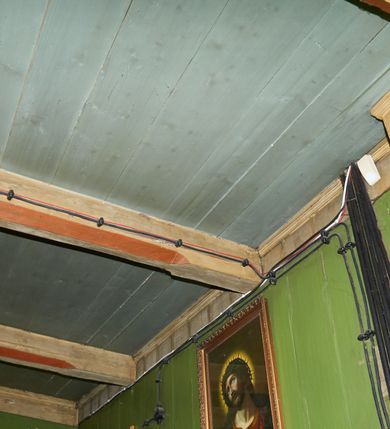 Zdjęcie nr 51: Polichromia ścian kościoła odpowiada podziałom architektonicznym wnętrza wydzielonym przez pilastry. Malowany zielony cokół w jednej czwartej wysokości ścian wyodrębniony jest pasem ornamentu geometrycznego, w nawie w jego polu znajdują się żółte prostokąty z dekoracją geometryczną, w prezbiterium malowana jasnozielona tkanina z dwoma pasami ornamentu roślinnego, medalionami z monogramami Marii i koronami oraz z motywem lilii heraldycznych i rozet. Trzony pilastrów wnętrza bladożółte z malowanymi płycinami dekorowanymi kampanulami, głowice zdobione malowanym kimationem. Na osi pilastrów, w partii fryzu, na tle niebieskich prostokątów uskrzydlone główki anielskie, pomiędzy nimi fryz wypełniony różowo-pomarańczowymi malowanymi płycinami w błękitnym obramieniu o fantazyjnym wykroju, dekorowanymi kampanulami. Belkowanie zamknięte malowanym pasem ornamentu geometrycznego. W polach pomiędzy pilastrami malowane płyciny o fantazyjnym kształcie zbliżonym do prostokąta, ujęte ramą zakończoną kartuszem, ich pola wypełnione są dekoracją geometryczną składającą się z krzyży równoramiennych w glorii i rozet wykonanych techniką patronową. Otwory okienne ujęte są malowanymi, imitującymi profilowanie obramieniami, otwory drzwiowe iluzjonistycznymi portalami z uszakami: portal w nawie zwieńczony jest kartuszem, a portal w prezbiterium zwieńczony jest szczytem zamkniętym fragmentem gzymsu w formie łuku segmentowego nadwieszonego podtrzymywanym przez spływy wolutowe. Pod chórem muzycznym malowane tablice pamiątkowe ujęte ramą, na ścianie północnej z napisem: „Ecclam hanc sub titulo Assumptionis B.V. Mariae a strenuo / milite Wierzbięta in Branice et Ruszcza Haerede pimo in / Wola juxta fines villae Stryjów a D. 1386 fundatam decimis / ex praedio Branice a colonis Stryjów, Wola, cuius sors est Grabie / Szczurów Zymbrzeg et ibidem taberna cum duobus pratis ac lacubus / Orzek et Piotrek ditatam, proper alluviem Vistulae  curatus suus / in hunc locum, qui erat pratum Gruczyn, ecclae dotale transtulit, / Hac tandem post annos 356 collapsa, quam vides, A.R.D. Jacobus Cichoński, parochus Grabiensis a.D. 1742 in loco desolatae  novam erexit. / Consecravit Illmus ac Rmus Michaël Kunicki, Sufraganeus Eppus. / Cracoviensis, Abbas Clarae Tumbae a D. 1749. / Restauravit A.R.D. Josephus Raźny, parochus Grabiensis a.D. 1907. / e colectis parochianorum.”; na ścianie południowej z napisem: „Ku Pamięci! / Dzieci Moje Najmilsze - Ja Prastara Świątynia / Polska dziękuję Wam za serdeczną troskę / o mnie. Oto dzięki Waszym ofiarom Drodzy / Rodzice i Twoim wysiłkom Kochana Młodzieży / w r. 1959 odnowiło się moje oblicze - rozjaśniały /  moje ołtarze, a w r. 1960 zabrzmiał mój nowy / organ na większą chwałę Bożą. Ja Was za to / rodzę na nowo do życia łaski. Ja Was błogosławię / na życie rodzinne. Ja Was prowadzę ku Bogu. Ja / Was także żegnam poraz ostatni, gdy przechodzicie / z tego padołu płaczu do wieczności, aby / Was znowu powitać kiedyś w niebie.”. Na ścianie zachodniej, pod chórem, nad środkowym otworem przejściowym pozostałości dawnego iluzjonistycznego portalu z kartuszem herbowym. Na stropie prezbiterium wydzielone pole o kształcie powtarzającym plan prezbiterium, wewnątrz pole w formie kwadratu o wklęsłych narożach z wpisanym polem o fantazyjnym zarysie zbliżonym do owalu ze sceną Wniebowzięcia Najświętszej Marii Panny. W narożach owalne pola z czterema istotami apokaliptycznymi. Prosta belka tęczowa w kolorze zielonym, o profilowaniach w kolorze niebieskim i różowym, z napisem: „JEZU ZMIŁUJ SIĘ NAD NAMI”. Na stropie nawy prostokątne pole wydzielone grubym bladoróżowym obramieniem z płycinami o nieregularnym kształcie wypełnionymi kratką regencyjną i rozetami alternowanymi medalionami z rozetami, naroża dekorowane są wstęgą regencyjną i akantem. Wewnątrz pole o fantazyjnym wykroju zbliżonym do owalu ze sceną Koronacji Najświętszej Marii Panny, flankowane przez dwie malowane błękitne płyciny o nieregularnym kształcie wypełnione rozetkami. W narożach, w ozdobnych kartuszach herby Pogoni Litewskiej i Orła Białego.
