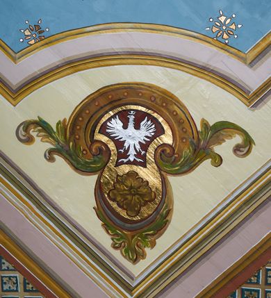 Zdjęcie nr 20: Polichromia ścian kościoła odpowiada podziałom architektonicznym wnętrza wydzielonym przez pilastry. Malowany zielony cokół w jednej czwartej wysokości ścian wyodrębniony jest pasem ornamentu geometrycznego, w nawie w jego polu znajdują się żółte prostokąty z dekoracją geometryczną, w prezbiterium malowana jasnozielona tkanina z dwoma pasami ornamentu roślinnego, medalionami z monogramami Marii i koronami oraz z motywem lilii heraldycznych i rozet. Trzony pilastrów wnętrza bladożółte z malowanymi płycinami dekorowanymi kampanulami, głowice zdobione malowanym kimationem. Na osi pilastrów, w partii fryzu, na tle niebieskich prostokątów uskrzydlone główki anielskie, pomiędzy nimi fryz wypełniony różowo-pomarańczowymi malowanymi płycinami w błękitnym obramieniu o fantazyjnym wykroju, dekorowanymi kampanulami. Belkowanie zamknięte malowanym pasem ornamentu geometrycznego. W polach pomiędzy pilastrami malowane płyciny o fantazyjnym kształcie zbliżonym do prostokąta, ujęte ramą zakończoną kartuszem, ich pola wypełnione są dekoracją geometryczną składającą się z krzyży równoramiennych w glorii i rozet wykonanych techniką patronową. Otwory okienne ujęte są malowanymi, imitującymi profilowanie obramieniami, otwory drzwiowe iluzjonistycznymi portalami z uszakami: portal w nawie zwieńczony jest kartuszem, a portal w prezbiterium zwieńczony jest szczytem zamkniętym fragmentem gzymsu w formie łuku segmentowego nadwieszonego podtrzymywanym przez spływy wolutowe. Pod chórem muzycznym malowane tablice pamiątkowe ujęte ramą, na ścianie północnej z napisem: „Ecclam hanc sub titulo Assumptionis B.V. Mariae a strenuo / milite Wierzbięta in Branice et Ruszcza Haerede pimo in / Wola juxta fines villae Stryjów a D. 1386 fundatam decimis / ex praedio Branice a colonis Stryjów, Wola, cuius sors est Grabie / Szczurów Zymbrzeg et ibidem taberna cum duobus pratis ac lacubus / Orzek et Piotrek ditatam, proper alluviem Vistulae  curatus suus / in hunc locum, qui erat pratum Gruczyn, ecclae dotale transtulit, / Hac tandem post annos 356 collapsa, quam vides, A.R.D. Jacobus Cichoński, parochus Grabiensis a.D. 1742 in loco desolatae  novam erexit. / Consecravit Illmus ac Rmus Michaël Kunicki, Sufraganeus Eppus. / Cracoviensis, Abbas Clarae Tumbae a D. 1749. / Restauravit A.R.D. Josephus Raźny, parochus Grabiensis a.D. 1907. / e colectis parochianorum.”; na ścianie południowej z napisem: „Ku Pamięci! / Dzieci Moje Najmilsze - Ja Prastara Świątynia / Polska dziękuję Wam za serdeczną troskę / o mnie. Oto dzięki Waszym ofiarom Drodzy / Rodzice i Twoim wysiłkom Kochana Młodzieży / w r. 1959 odnowiło się moje oblicze - rozjaśniały /  moje ołtarze, a w r. 1960 zabrzmiał mój nowy / organ na większą chwałę Bożą. Ja Was za to / rodzę na nowo do życia łaski. Ja Was błogosławię / na życie rodzinne. Ja Was prowadzę ku Bogu. Ja / Was także żegnam poraz ostatni, gdy przechodzicie / z tego padołu płaczu do wieczności, aby / Was znowu powitać kiedyś w niebie.”. Na ścianie zachodniej, pod chórem, nad środkowym otworem przejściowym pozostałości dawnego iluzjonistycznego portalu z kartuszem herbowym. Na stropie prezbiterium wydzielone pole o kształcie powtarzającym plan prezbiterium, wewnątrz pole w formie kwadratu o wklęsłych narożach z wpisanym polem o fantazyjnym zarysie zbliżonym do owalu ze sceną Wniebowzięcia Najświętszej Marii Panny. W narożach owalne pola z czterema istotami apokaliptycznymi. Prosta belka tęczowa w kolorze zielonym, o profilowaniach w kolorze niebieskim i różowym, z napisem: „JEZU ZMIŁUJ SIĘ NAD NAMI”. Na stropie nawy prostokątne pole wydzielone grubym bladoróżowym obramieniem z płycinami o nieregularnym kształcie wypełnionymi kratką regencyjną i rozetami alternowanymi medalionami z rozetami, naroża dekorowane są wstęgą regencyjną i akantem. Wewnątrz pole o fantazyjnym wykroju zbliżonym do owalu ze sceną Koronacji Najświętszej Marii Panny, flankowane przez dwie malowane błękitne płyciny o nieregularnym kształcie wypełnione rozetkami. W narożach, w ozdobnych kartuszach herby Pogoni Litewskiej i Orła Białego.
