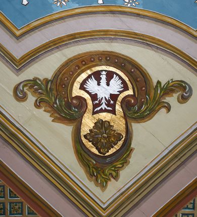 Zdjęcie nr 23: Polichromia ścian kościoła odpowiada podziałom architektonicznym wnętrza wydzielonym przez pilastry. Malowany zielony cokół w jednej czwartej wysokości ścian wyodrębniony jest pasem ornamentu geometrycznego, w nawie w jego polu znajdują się żółte prostokąty z dekoracją geometryczną, w prezbiterium malowana jasnozielona tkanina z dwoma pasami ornamentu roślinnego, medalionami z monogramami Marii i koronami oraz z motywem lilii heraldycznych i rozet. Trzony pilastrów wnętrza bladożółte z malowanymi płycinami dekorowanymi kampanulami, głowice zdobione malowanym kimationem. Na osi pilastrów, w partii fryzu, na tle niebieskich prostokątów uskrzydlone główki anielskie, pomiędzy nimi fryz wypełniony różowo-pomarańczowymi malowanymi płycinami w błękitnym obramieniu o fantazyjnym wykroju, dekorowanymi kampanulami. Belkowanie zamknięte malowanym pasem ornamentu geometrycznego. W polach pomiędzy pilastrami malowane płyciny o fantazyjnym kształcie zbliżonym do prostokąta, ujęte ramą zakończoną kartuszem, ich pola wypełnione są dekoracją geometryczną składającą się z krzyży równoramiennych w glorii i rozet wykonanych techniką patronową. Otwory okienne ujęte są malowanymi, imitującymi profilowanie obramieniami, otwory drzwiowe iluzjonistycznymi portalami z uszakami: portal w nawie zwieńczony jest kartuszem, a portal w prezbiterium zwieńczony jest szczytem zamkniętym fragmentem gzymsu w formie łuku segmentowego nadwieszonego podtrzymywanym przez spływy wolutowe. Pod chórem muzycznym malowane tablice pamiątkowe ujęte ramą, na ścianie północnej z napisem: „Ecclam hanc sub titulo Assumptionis B.V. Mariae a strenuo / milite Wierzbięta in Branice et Ruszcza Haerede pimo in / Wola juxta fines villae Stryjów a D. 1386 fundatam decimis / ex praedio Branice a colonis Stryjów, Wola, cuius sors est Grabie / Szczurów Zymbrzeg et ibidem taberna cum duobus pratis ac lacubus / Orzek et Piotrek ditatam, proper alluviem Vistulae  curatus suus / in hunc locum, qui erat pratum Gruczyn, ecclae dotale transtulit, / Hac tandem post annos 356 collapsa, quam vides, A.R.D. Jacobus Cichoński, parochus Grabiensis a.D. 1742 in loco desolatae  novam erexit. / Consecravit Illmus ac Rmus Michaël Kunicki, Sufraganeus Eppus. / Cracoviensis, Abbas Clarae Tumbae a D. 1749. / Restauravit A.R.D. Josephus Raźny, parochus Grabiensis a.D. 1907. / e colectis parochianorum.”; na ścianie południowej z napisem: „Ku Pamięci! / Dzieci Moje Najmilsze - Ja Prastara Świątynia / Polska dziękuję Wam za serdeczną troskę / o mnie. Oto dzięki Waszym ofiarom Drodzy / Rodzice i Twoim wysiłkom Kochana Młodzieży / w r. 1959 odnowiło się moje oblicze - rozjaśniały /  moje ołtarze, a w r. 1960 zabrzmiał mój nowy / organ na większą chwałę Bożą. Ja Was za to / rodzę na nowo do życia łaski. Ja Was błogosławię / na życie rodzinne. Ja Was prowadzę ku Bogu. Ja / Was także żegnam poraz ostatni, gdy przechodzicie / z tego padołu płaczu do wieczności, aby / Was znowu powitać kiedyś w niebie.”. Na ścianie zachodniej, pod chórem, nad środkowym otworem przejściowym pozostałości dawnego iluzjonistycznego portalu z kartuszem herbowym. Na stropie prezbiterium wydzielone pole o kształcie powtarzającym plan prezbiterium, wewnątrz pole w formie kwadratu o wklęsłych narożach z wpisanym polem o fantazyjnym zarysie zbliżonym do owalu ze sceną Wniebowzięcia Najświętszej Marii Panny. W narożach owalne pola z czterema istotami apokaliptycznymi. Prosta belka tęczowa w kolorze zielonym, o profilowaniach w kolorze niebieskim i różowym, z napisem: „JEZU ZMIŁUJ SIĘ NAD NAMI”. Na stropie nawy prostokątne pole wydzielone grubym bladoróżowym obramieniem z płycinami o nieregularnym kształcie wypełnionymi kratką regencyjną i rozetami alternowanymi medalionami z rozetami, naroża dekorowane są wstęgą regencyjną i akantem. Wewnątrz pole o fantazyjnym wykroju zbliżonym do owalu ze sceną Koronacji Najświętszej Marii Panny, flankowane przez dwie malowane błękitne płyciny o nieregularnym kształcie wypełnione rozetkami. W narożach, w ozdobnych kartuszach herby Pogoni Litewskiej i Orła Białego.
