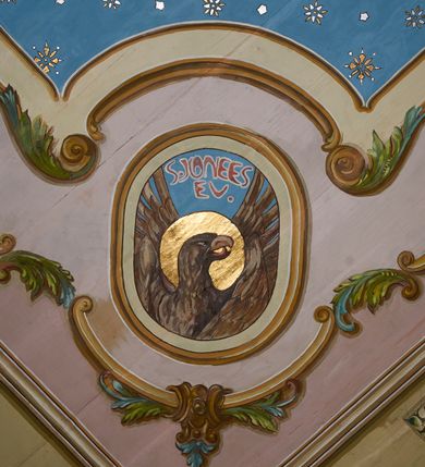 Zdjęcie nr 40: Polichromia ścian kościoła odpowiada podziałom architektonicznym wnętrza wydzielonym przez pilastry. Malowany zielony cokół w jednej czwartej wysokości ścian wyodrębniony jest pasem ornamentu geometrycznego, w nawie w jego polu znajdują się żółte prostokąty z dekoracją geometryczną, w prezbiterium malowana jasnozielona tkanina z dwoma pasami ornamentu roślinnego, medalionami z monogramami Marii i koronami oraz z motywem lilii heraldycznych i rozet. Trzony pilastrów wnętrza bladożółte z malowanymi płycinami dekorowanymi kampanulami, głowice zdobione malowanym kimationem. Na osi pilastrów, w partii fryzu, na tle niebieskich prostokątów uskrzydlone główki anielskie, pomiędzy nimi fryz wypełniony różowo-pomarańczowymi malowanymi płycinami w błękitnym obramieniu o fantazyjnym wykroju, dekorowanymi kampanulami. Belkowanie zamknięte malowanym pasem ornamentu geometrycznego. W polach pomiędzy pilastrami malowane płyciny o fantazyjnym kształcie zbliżonym do prostokąta, ujęte ramą zakończoną kartuszem, ich pola wypełnione są dekoracją geometryczną składającą się z krzyży równoramiennych w glorii i rozet wykonanych techniką patronową. Otwory okienne ujęte są malowanymi, imitującymi profilowanie obramieniami, otwory drzwiowe iluzjonistycznymi portalami z uszakami: portal w nawie zwieńczony jest kartuszem, a portal w prezbiterium zwieńczony jest szczytem zamkniętym fragmentem gzymsu w formie łuku segmentowego nadwieszonego podtrzymywanym przez spływy wolutowe. Pod chórem muzycznym malowane tablice pamiątkowe ujęte ramą, na ścianie północnej z napisem: „Ecclam hanc sub titulo Assumptionis B.V. Mariae a strenuo / milite Wierzbięta in Branice et Ruszcza Haerede pimo in / Wola juxta fines villae Stryjów a D. 1386 fundatam decimis / ex praedio Branice a colonis Stryjów, Wola, cuius sors est Grabie / Szczurów Zymbrzeg et ibidem taberna cum duobus pratis ac lacubus / Orzek et Piotrek ditatam, proper alluviem Vistulae  curatus suus / in hunc locum, qui erat pratum Gruczyn, ecclae dotale transtulit, / Hac tandem post annos 356 collapsa, quam vides, A.R.D. Jacobus Cichoński, parochus Grabiensis a.D. 1742 in loco desolatae  novam erexit. / Consecravit Illmus ac Rmus Michaël Kunicki, Sufraganeus Eppus. / Cracoviensis, Abbas Clarae Tumbae a D. 1749. / Restauravit A.R.D. Josephus Raźny, parochus Grabiensis a.D. 1907. / e colectis parochianorum.”; na ścianie południowej z napisem: „Ku Pamięci! / Dzieci Moje Najmilsze - Ja Prastara Świątynia / Polska dziękuję Wam za serdeczną troskę / o mnie. Oto dzięki Waszym ofiarom Drodzy / Rodzice i Twoim wysiłkom Kochana Młodzieży / w r. 1959 odnowiło się moje oblicze - rozjaśniały /  moje ołtarze, a w r. 1960 zabrzmiał mój nowy / organ na większą chwałę Bożą. Ja Was za to / rodzę na nowo do życia łaski. Ja Was błogosławię / na życie rodzinne. Ja Was prowadzę ku Bogu. Ja / Was także żegnam poraz ostatni, gdy przechodzicie / z tego padołu płaczu do wieczności, aby / Was znowu powitać kiedyś w niebie.”. Na ścianie zachodniej, pod chórem, nad środkowym otworem przejściowym pozostałości dawnego iluzjonistycznego portalu z kartuszem herbowym. Na stropie prezbiterium wydzielone pole o kształcie powtarzającym plan prezbiterium, wewnątrz pole w formie kwadratu o wklęsłych narożach z wpisanym polem o fantazyjnym zarysie zbliżonym do owalu ze sceną Wniebowzięcia Najświętszej Marii Panny. W narożach owalne pola z czterema istotami apokaliptycznymi. Prosta belka tęczowa w kolorze zielonym, o profilowaniach w kolorze niebieskim i różowym, z napisem: „JEZU ZMIŁUJ SIĘ NAD NAMI”. Na stropie nawy prostokątne pole wydzielone grubym bladoróżowym obramieniem z płycinami o nieregularnym kształcie wypełnionymi kratką regencyjną i rozetami alternowanymi medalionami z rozetami, naroża dekorowane są wstęgą regencyjną i akantem. Wewnątrz pole o fantazyjnym wykroju zbliżonym do owalu ze sceną Koronacji Najświętszej Marii Panny, flankowane przez dwie malowane błękitne płyciny o nieregularnym kształcie wypełnione rozetkami. W narożach, w ozdobnych kartuszach herby Pogoni Litewskiej i Orła Białego.
