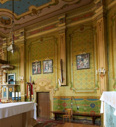 Zdjęcie nr 45: Polichromia ścian kościoła odpowiada podziałom architektonicznym wnętrza wydzielonym przez pilastry. Malowany zielony cokół w jednej czwartej wysokości ścian wyodrębniony jest pasem ornamentu geometrycznego, w nawie w jego polu znajdują się żółte prostokąty z dekoracją geometryczną, w prezbiterium malowana jasnozielona tkanina z dwoma pasami ornamentu roślinnego, medalionami z monogramami Marii i koronami oraz z motywem lilii heraldycznych i rozet. Trzony pilastrów wnętrza bladożółte z malowanymi płycinami dekorowanymi kampanulami, głowice zdobione malowanym kimationem. Na osi pilastrów, w partii fryzu, na tle niebieskich prostokątów uskrzydlone główki anielskie, pomiędzy nimi fryz wypełniony różowo-pomarańczowymi malowanymi płycinami w błękitnym obramieniu o fantazyjnym wykroju, dekorowanymi kampanulami. Belkowanie zamknięte malowanym pasem ornamentu geometrycznego. W polach pomiędzy pilastrami malowane płyciny o fantazyjnym kształcie zbliżonym do prostokąta, ujęte ramą zakończoną kartuszem, ich pola wypełnione są dekoracją geometryczną składającą się z krzyży równoramiennych w glorii i rozet wykonanych techniką patronową. Otwory okienne ujęte są malowanymi, imitującymi profilowanie obramieniami, otwory drzwiowe iluzjonistycznymi portalami z uszakami: portal w nawie zwieńczony jest kartuszem, a portal w prezbiterium zwieńczony jest szczytem zamkniętym fragmentem gzymsu w formie łuku segmentowego nadwieszonego podtrzymywanym przez spływy wolutowe. Pod chórem muzycznym malowane tablice pamiątkowe ujęte ramą, na ścianie północnej z napisem: „Ecclam hanc sub titulo Assumptionis B.V. Mariae a strenuo / milite Wierzbięta in Branice et Ruszcza Haerede pimo in / Wola juxta fines villae Stryjów a D. 1386 fundatam decimis / ex praedio Branice a colonis Stryjów, Wola, cuius sors est Grabie / Szczurów Zymbrzeg et ibidem taberna cum duobus pratis ac lacubus / Orzek et Piotrek ditatam, proper alluviem Vistulae  curatus suus / in hunc locum, qui erat pratum Gruczyn, ecclae dotale transtulit, / Hac tandem post annos 356 collapsa, quam vides, A.R.D. Jacobus Cichoński, parochus Grabiensis a.D. 1742 in loco desolatae  novam erexit. / Consecravit Illmus ac Rmus Michaël Kunicki, Sufraganeus Eppus. / Cracoviensis, Abbas Clarae Tumbae a D. 1749. / Restauravit A.R.D. Josephus Raźny, parochus Grabiensis a.D. 1907. / e colectis parochianorum.”; na ścianie południowej z napisem: „Ku Pamięci! / Dzieci Moje Najmilsze - Ja Prastara Świątynia / Polska dziękuję Wam za serdeczną troskę / o mnie. Oto dzięki Waszym ofiarom Drodzy / Rodzice i Twoim wysiłkom Kochana Młodzieży / w r. 1959 odnowiło się moje oblicze - rozjaśniały /  moje ołtarze, a w r. 1960 zabrzmiał mój nowy / organ na większą chwałę Bożą. Ja Was za to / rodzę na nowo do życia łaski. Ja Was błogosławię / na życie rodzinne. Ja Was prowadzę ku Bogu. Ja / Was także żegnam poraz ostatni, gdy przechodzicie / z tego padołu płaczu do wieczności, aby / Was znowu powitać kiedyś w niebie.”. Na ścianie zachodniej, pod chórem, nad środkowym otworem przejściowym pozostałości dawnego iluzjonistycznego portalu z kartuszem herbowym. Na stropie prezbiterium wydzielone pole o kształcie powtarzającym plan prezbiterium, wewnątrz pole w formie kwadratu o wklęsłych narożach z wpisanym polem o fantazyjnym zarysie zbliżonym do owalu ze sceną Wniebowzięcia Najświętszej Marii Panny. W narożach owalne pola z czterema istotami apokaliptycznymi. Prosta belka tęczowa w kolorze zielonym, o profilowaniach w kolorze niebieskim i różowym, z napisem: „JEZU ZMIŁUJ SIĘ NAD NAMI”. Na stropie nawy prostokątne pole wydzielone grubym bladoróżowym obramieniem z płycinami o nieregularnym kształcie wypełnionymi kratką regencyjną i rozetami alternowanymi medalionami z rozetami, naroża dekorowane są wstęgą regencyjną i akantem. Wewnątrz pole o fantazyjnym wykroju zbliżonym do owalu ze sceną Koronacji Najświętszej Marii Panny, flankowane przez dwie malowane błękitne płyciny o nieregularnym kształcie wypełnione rozetkami. W narożach, w ozdobnych kartuszach herby Pogoni Litewskiej i Orła Białego.
