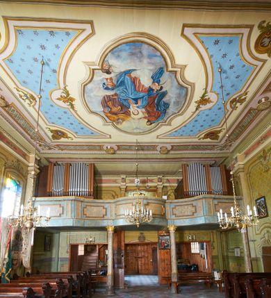 Zdjęcie nr 32: Polichromia ścian kościoła odpowiada podziałom architektonicznym wnętrza wydzielonym przez pilastry. Malowany zielony cokół w jednej czwartej wysokości ścian wyodrębniony jest pasem ornamentu geometrycznego, w nawie w jego polu znajdują się żółte prostokąty z dekoracją geometryczną, w prezbiterium malowana jasnozielona tkanina z dwoma pasami ornamentu roślinnego, medalionami z monogramami Marii i koronami oraz z motywem lilii heraldycznych i rozet. Trzony pilastrów wnętrza bladożółte z malowanymi płycinami dekorowanymi kampanulami, głowice zdobione malowanym kimationem. Na osi pilastrów, w partii fryzu, na tle niebieskich prostokątów uskrzydlone główki anielskie, pomiędzy nimi fryz wypełniony różowo-pomarańczowymi malowanymi płycinami w błękitnym obramieniu o fantazyjnym wykroju, dekorowanymi kampanulami. Belkowanie zamknięte malowanym pasem ornamentu geometrycznego. W polach pomiędzy pilastrami malowane płyciny o fantazyjnym kształcie zbliżonym do prostokąta, ujęte ramą zakończoną kartuszem, ich pola wypełnione są dekoracją geometryczną składającą się z krzyży równoramiennych w glorii i rozet wykonanych techniką patronową. Otwory okienne ujęte są malowanymi, imitującymi profilowanie obramieniami, otwory drzwiowe iluzjonistycznymi portalami z uszakami: portal w nawie zwieńczony jest kartuszem, a portal w prezbiterium zwieńczony jest szczytem zamkniętym fragmentem gzymsu w formie łuku segmentowego nadwieszonego podtrzymywanym przez spływy wolutowe. Pod chórem muzycznym malowane tablice pamiątkowe ujęte ramą, na ścianie północnej z napisem: „Ecclam hanc sub titulo Assumptionis B.V. Mariae a strenuo / milite Wierzbięta in Branice et Ruszcza Haerede pimo in / Wola juxta fines villae Stryjów a D. 1386 fundatam decimis / ex praedio Branice a colonis Stryjów, Wola, cuius sors est Grabie / Szczurów Zymbrzeg et ibidem taberna cum duobus pratis ac lacubus / Orzek et Piotrek ditatam, proper alluviem Vistulae  curatus suus / in hunc locum, qui erat pratum Gruczyn, ecclae dotale transtulit, / Hac tandem post annos 356 collapsa, quam vides, A.R.D. Jacobus Cichoński, parochus Grabiensis a.D. 1742 in loco desolatae  novam erexit. / Consecravit Illmus ac Rmus Michaël Kunicki, Sufraganeus Eppus. / Cracoviensis, Abbas Clarae Tumbae a D. 1749. / Restauravit A.R.D. Josephus Raźny, parochus Grabiensis a.D. 1907. / e colectis parochianorum.”; na ścianie południowej z napisem: „Ku Pamięci! / Dzieci Moje Najmilsze - Ja Prastara Świątynia / Polska dziękuję Wam za serdeczną troskę / o mnie. Oto dzięki Waszym ofiarom Drodzy / Rodzice i Twoim wysiłkom Kochana Młodzieży / w r. 1959 odnowiło się moje oblicze - rozjaśniały /  moje ołtarze, a w r. 1960 zabrzmiał mój nowy / organ na większą chwałę Bożą. Ja Was za to / rodzę na nowo do życia łaski. Ja Was błogosławię / na życie rodzinne. Ja Was prowadzę ku Bogu. Ja / Was także żegnam poraz ostatni, gdy przechodzicie / z tego padołu płaczu do wieczności, aby / Was znowu powitać kiedyś w niebie.”. Na ścianie zachodniej, pod chórem, nad środkowym otworem przejściowym pozostałości dawnego iluzjonistycznego portalu z kartuszem herbowym. Na stropie prezbiterium wydzielone pole o kształcie powtarzającym plan prezbiterium, wewnątrz pole w formie kwadratu o wklęsłych narożach z wpisanym polem o fantazyjnym zarysie zbliżonym do owalu ze sceną Wniebowzięcia Najświętszej Marii Panny. W narożach owalne pola z czterema istotami apokaliptycznymi. Prosta belka tęczowa w kolorze zielonym, o profilowaniach w kolorze niebieskim i różowym, z napisem: „JEZU ZMIŁUJ SIĘ NAD NAMI”. Na stropie nawy prostokątne pole wydzielone grubym bladoróżowym obramieniem z płycinami o nieregularnym kształcie wypełnionymi kratką regencyjną i rozetami alternowanymi medalionami z rozetami, naroża dekorowane są wstęgą regencyjną i akantem. Wewnątrz pole o fantazyjnym wykroju zbliżonym do owalu ze sceną Koronacji Najświętszej Marii Panny, flankowane przez dwie malowane błękitne płyciny o nieregularnym kształcie wypełnione rozetkami. W narożach, w ozdobnych kartuszach herby Pogoni Litewskiej i Orła Białego.
