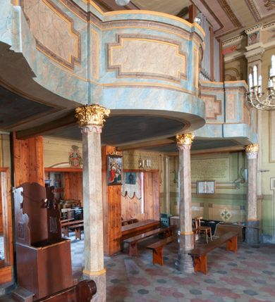 Zdjęcie nr 9: Polichromia ścian kościoła odpowiada podziałom architektonicznym wnętrza wydzielonym przez pilastry. Malowany zielony cokół w jednej czwartej wysokości ścian wyodrębniony jest pasem ornamentu geometrycznego, w nawie w jego polu znajdują się żółte prostokąty z dekoracją geometryczną, w prezbiterium malowana jasnozielona tkanina z dwoma pasami ornamentu roślinnego, medalionami z monogramami Marii i koronami oraz z motywem lilii heraldycznych i rozet. Trzony pilastrów wnętrza bladożółte z malowanymi płycinami dekorowanymi kampanulami, głowice zdobione malowanym kimationem. Na osi pilastrów, w partii fryzu, na tle niebieskich prostokątów uskrzydlone główki anielskie, pomiędzy nimi fryz wypełniony różowo-pomarańczowymi malowanymi płycinami w błękitnym obramieniu o fantazyjnym wykroju, dekorowanymi kampanulami. Belkowanie zamknięte malowanym pasem ornamentu geometrycznego. W polach pomiędzy pilastrami malowane płyciny o fantazyjnym kształcie zbliżonym do prostokąta, ujęte ramą zakończoną kartuszem, ich pola wypełnione są dekoracją geometryczną składającą się z krzyży równoramiennych w glorii i rozet wykonanych techniką patronową. Otwory okienne ujęte są malowanymi, imitującymi profilowanie obramieniami, otwory drzwiowe iluzjonistycznymi portalami z uszakami: portal w nawie zwieńczony jest kartuszem, a portal w prezbiterium zwieńczony jest szczytem zamkniętym fragmentem gzymsu w formie łuku segmentowego nadwieszonego podtrzymywanym przez spływy wolutowe. Pod chórem muzycznym malowane tablice pamiątkowe ujęte ramą, na ścianie północnej z napisem: „Ecclam hanc sub titulo Assumptionis B.V. Mariae a strenuo / milite Wierzbięta in Branice et Ruszcza Haerede pimo in / Wola juxta fines villae Stryjów a D. 1386 fundatam decimis / ex praedio Branice a colonis Stryjów, Wola, cuius sors est Grabie / Szczurów Zymbrzeg et ibidem taberna cum duobus pratis ac lacubus / Orzek et Piotrek ditatam, proper alluviem Vistulae  curatus suus / in hunc locum, qui erat pratum Gruczyn, ecclae dotale transtulit, / Hac tandem post annos 356 collapsa, quam vides, A.R.D. Jacobus Cichoński, parochus Grabiensis a.D. 1742 in loco desolatae  novam erexit. / Consecravit Illmus ac Rmus Michaël Kunicki, Sufraganeus Eppus. / Cracoviensis, Abbas Clarae Tumbae a D. 1749. / Restauravit A.R.D. Josephus Raźny, parochus Grabiensis a.D. 1907. / e colectis parochianorum.”; na ścianie południowej z napisem: „Ku Pamięci! / Dzieci Moje Najmilsze - Ja Prastara Świątynia / Polska dziękuję Wam za serdeczną troskę / o mnie. Oto dzięki Waszym ofiarom Drodzy / Rodzice i Twoim wysiłkom Kochana Młodzieży / w r. 1959 odnowiło się moje oblicze - rozjaśniały /  moje ołtarze, a w r. 1960 zabrzmiał mój nowy / organ na większą chwałę Bożą. Ja Was za to / rodzę na nowo do życia łaski. Ja Was błogosławię / na życie rodzinne. Ja Was prowadzę ku Bogu. Ja / Was także żegnam poraz ostatni, gdy przechodzicie / z tego padołu płaczu do wieczności, aby / Was znowu powitać kiedyś w niebie.”. Na ścianie zachodniej, pod chórem, nad środkowym otworem przejściowym pozostałości dawnego iluzjonistycznego portalu z kartuszem herbowym. Na stropie prezbiterium wydzielone pole o kształcie powtarzającym plan prezbiterium, wewnątrz pole w formie kwadratu o wklęsłych narożach z wpisanym polem o fantazyjnym zarysie zbliżonym do owalu ze sceną Wniebowzięcia Najświętszej Marii Panny. W narożach owalne pola z czterema istotami apokaliptycznymi. Prosta belka tęczowa w kolorze zielonym, o profilowaniach w kolorze niebieskim i różowym, z napisem: „JEZU ZMIŁUJ SIĘ NAD NAMI”. Na stropie nawy prostokątne pole wydzielone grubym bladoróżowym obramieniem z płycinami o nieregularnym kształcie wypełnionymi kratką regencyjną i rozetami alternowanymi medalionami z rozetami, naroża dekorowane są wstęgą regencyjną i akantem. Wewnątrz pole o fantazyjnym wykroju zbliżonym do owalu ze sceną Koronacji Najświętszej Marii Panny, flankowane przez dwie malowane błękitne płyciny o nieregularnym kształcie wypełnione rozetkami. W narożach, w ozdobnych kartuszach herby Pogoni Litewskiej i Orła Białego.
