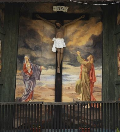 Zdjęcie nr 1: Na zewnętrznej stronie prezbiterium znajduje się ogrójec, który zamknięty jest trzema ścianami, otwarty od frontu i przegrodzony balustradą, zamknięty od góry zadaszeniem. Na północnej i południowej ścianie znajdują się po trzy pola w malowanych prześwitach, dwa dolne wypełniają sceny męki Chrystusa, w najwyższych przedstawiono zachmurzone niebo. Scena główna znajduje się na wschodniej ścianie prezbiterium i złożona jest z rzeźbionego krucyfiksu oraz malowanego tła. Cykl przedstawień męki Pańskiej rozpoczyna się na ścianie południowej. Scena pierwsza cyklu – Modlitwa w Ogrójcu, usytuowana jest w środkowym polu ściany. Ilustruje klęczącego na tle pejzażu przed skałą Chrystusa, przed którym w promieniach światła unosi się anioł trzymający kielich. W prawej części przedstawienia, w tle ukazani są dwaj śpiący apostołowie. Scena druga, Biczowanie, usytuowana jest w najniższym polu ściany południowej, przedstawia wnętrze z kamiennymi ścianami. W jej prawej części znajduje się na wpół leżący i oparty o słup Chrystus ze związanymi rękami, przepasany czerwoną szatą z koroną cierniową na głowie. W lewej części przedstawiony jest oprawca, ukazany tyłem, opierający się lewą nogą o ciało Jezusa i zamachujący się na niego biczem. Kolejne przedstawienia z cyklu znajdują się na północnej ścianie. Kontynuuje go trzecia scena – Koronowanie cierniem, znajdująca się w najniższym polu. Ukazuje wnętrze z niebieską kotarą w tle, w lewej części przedstawiony jest siedzący frontalnie Chrystus w czerwonym płaszczu, za nim zaś mężczyzna, nakładający na jego głowę koronę cierniową. W prawej części na pierwszym planie znajdują się mężczyźni naigrywający się z Jezusa i składający mu pokłon, z tyłu postać żołnierza. Scena czwarta to Droga Krzyżowa, usytuowana jest w środkowym polu ściany północnej. Ilustruje upadek Chrystusa niosącego krzyż i Szymona Cyrenejczyka, który pomaga mu go podnieść. W tle pejzaż z tłumem ludzi i żołnierzami. Scena główna przedstawia Ukrzyżowanie z Marią i św. Janem. W centrum znajduje się krzyż z figurą umarłego Chrystusa na tle malowanego pustynno-górzystego pejzażu z Jerozolimą oraz ze skłębionym żółto-błękitnym niebem. Po lewej stronie krzyża Matka Boska zwrócona w trzech czwartych w prawo, lewą ręką wskazuje na krzyż, prawą składa na piersi. Ubrana jest w czerwoną suknię i niebieski płaszcz narzucony na głowę. Po prawej stronie krzyża św. Jan ukazany z profilu, prawą nogą oparty o skałę, wznosi ku górze splecione dłonie w geście rozpaczy. Ubrany w zieloną suknię, przepasaną w talii oraz czerwony płaszcz. Wnętrze kapliczki pomalowane jest na kolor jasnozielony. 


