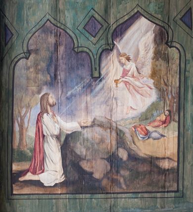 Zdjęcie nr 18: Na zewnętrznej stronie prezbiterium znajduje się ogrójec, który zamknięty jest trzema ścianami, otwarty od frontu i przegrodzony balustradą, zamknięty od góry zadaszeniem. Na północnej i południowej ścianie znajdują się po trzy pola w malowanych prześwitach, dwa dolne wypełniają sceny męki Chrystusa, w najwyższych przedstawiono zachmurzone niebo. Scena główna znajduje się na wschodniej ścianie prezbiterium i złożona jest z rzeźbionego krucyfiksu oraz malowanego tła. Cykl przedstawień męki Pańskiej rozpoczyna się na ścianie południowej. Scena pierwsza cyklu – Modlitwa w Ogrójcu, usytuowana jest w środkowym polu ściany. Ilustruje klęczącego na tle pejzażu przed skałą Chrystusa, przed którym w promieniach światła unosi się anioł trzymający kielich. W prawej części przedstawienia, w tle ukazani są dwaj śpiący apostołowie. Scena druga, Biczowanie, usytuowana jest w najniższym polu ściany południowej, przedstawia wnętrze z kamiennymi ścianami. W jej prawej części znajduje się na wpół leżący i oparty o słup Chrystus ze związanymi rękami, przepasany czerwoną szatą z koroną cierniową na głowie. W lewej części przedstawiony jest oprawca, ukazany tyłem, opierający się lewą nogą o ciało Jezusa i zamachujący się na niego biczem. Kolejne przedstawienia z cyklu znajdują się na północnej ścianie. Kontynuuje go trzecia scena – Koronowanie cierniem, znajdująca się w najniższym polu. Ukazuje wnętrze z niebieską kotarą w tle, w lewej części przedstawiony jest siedzący frontalnie Chrystus w czerwonym płaszczu, za nim zaś mężczyzna, nakładający na jego głowę koronę cierniową. W prawej części na pierwszym planie znajdują się mężczyźni naigrywający się z Jezusa i składający mu pokłon, z tyłu postać żołnierza. Scena czwarta to Droga Krzyżowa, usytuowana jest w środkowym polu ściany północnej. Ilustruje upadek Chrystusa niosącego krzyż i Szymona Cyrenejczyka, który pomaga mu go podnieść. W tle pejzaż z tłumem ludzi i żołnierzami. Scena główna przedstawia Ukrzyżowanie z Marią i św. Janem. W centrum znajduje się krzyż z figurą umarłego Chrystusa na tle malowanego pustynno-górzystego pejzażu z Jerozolimą oraz ze skłębionym żółto-błękitnym niebem. Po lewej stronie krzyża Matka Boska zwrócona w trzech czwartych w prawo, lewą ręką wskazuje na krzyż, prawą składa na piersi. Ubrana jest w czerwoną suknię i niebieski płaszcz narzucony na głowę. Po prawej stronie krzyża św. Jan ukazany z profilu, prawą nogą oparty o skałę, wznosi ku górze splecione dłonie w geście rozpaczy. Ubrany w zieloną suknię, przepasaną w talii oraz czerwony płaszcz. Wnętrze kapliczki pomalowane jest na kolor jasnozielony. 


