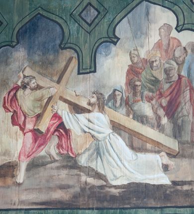 Zdjęcie nr 8: Na zewnętrznej stronie prezbiterium znajduje się ogrójec, który zamknięty jest trzema ścianami, otwarty od frontu i przegrodzony balustradą, zamknięty od góry zadaszeniem. Na północnej i południowej ścianie znajdują się po trzy pola w malowanych prześwitach, dwa dolne wypełniają sceny męki Chrystusa, w najwyższych przedstawiono zachmurzone niebo. Scena główna znajduje się na wschodniej ścianie prezbiterium i złożona jest z rzeźbionego krucyfiksu oraz malowanego tła. Cykl przedstawień męki Pańskiej rozpoczyna się na ścianie południowej. Scena pierwsza cyklu – Modlitwa w Ogrójcu, usytuowana jest w środkowym polu ściany. Ilustruje klęczącego na tle pejzażu przed skałą Chrystusa, przed którym w promieniach światła unosi się anioł trzymający kielich. W prawej części przedstawienia, w tle ukazani są dwaj śpiący apostołowie. Scena druga, Biczowanie, usytuowana jest w najniższym polu ściany południowej, przedstawia wnętrze z kamiennymi ścianami. W jej prawej części znajduje się na wpół leżący i oparty o słup Chrystus ze związanymi rękami, przepasany czerwoną szatą z koroną cierniową na głowie. W lewej części przedstawiony jest oprawca, ukazany tyłem, opierający się lewą nogą o ciało Jezusa i zamachujący się na niego biczem. Kolejne przedstawienia z cyklu znajdują się na północnej ścianie. Kontynuuje go trzecia scena – Koronowanie cierniem, znajdująca się w najniższym polu. Ukazuje wnętrze z niebieską kotarą w tle, w lewej części przedstawiony jest siedzący frontalnie Chrystus w czerwonym płaszczu, za nim zaś mężczyzna, nakładający na jego głowę koronę cierniową. W prawej części na pierwszym planie znajdują się mężczyźni naigrywający się z Jezusa i składający mu pokłon, z tyłu postać żołnierza. Scena czwarta to Droga Krzyżowa, usytuowana jest w środkowym polu ściany północnej. Ilustruje upadek Chrystusa niosącego krzyż i Szymona Cyrenejczyka, który pomaga mu go podnieść. W tle pejzaż z tłumem ludzi i żołnierzami. Scena główna przedstawia Ukrzyżowanie z Marią i św. Janem. W centrum znajduje się krzyż z figurą umarłego Chrystusa na tle malowanego pustynno-górzystego pejzażu z Jerozolimą oraz ze skłębionym żółto-błękitnym niebem. Po lewej stronie krzyża Matka Boska zwrócona w trzech czwartych w prawo, lewą ręką wskazuje na krzyż, prawą składa na piersi. Ubrana jest w czerwoną suknię i niebieski płaszcz narzucony na głowę. Po prawej stronie krzyża św. Jan ukazany z profilu, prawą nogą oparty o skałę, wznosi ku górze splecione dłonie w geście rozpaczy. Ubrany w zieloną suknię, przepasaną w talii oraz czerwony płaszcz. Wnętrze kapliczki pomalowane jest na kolor jasnozielony. 


