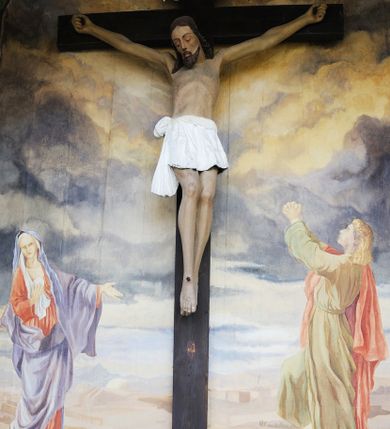 Zdjęcie nr 1: Figura Chrystusa umarłego, przybita jest do prostego krzyża trzema gwoździami. Ukazana została w lekkim zwisie ciała, o szeroko rozpostartych ramionach z zaciśniętymi dłońmi, nogi są delikatnie ugięte w kolanach, a stopy w układzie prawa na lewą. Twarz pociągła o wyraźnych rysach łuków brwiowych i prostego nosa, oczy są zamknięte. Okolona jest brodą oraz włosami opadającymi na ramiona. Ciało jest wychudzone, o delikatnym modelunku klatki piersiowej, z podkreślonymi mięśniami ramion wyłamanych z barków. Białe perizonium sięgające połowy ud, zawiązane jest na prawym biodrze ze zwisem tkaniny. Polichromia ciała naturalistyczna z delikatnie zaznaczonymi krwawiącymi ranami. 