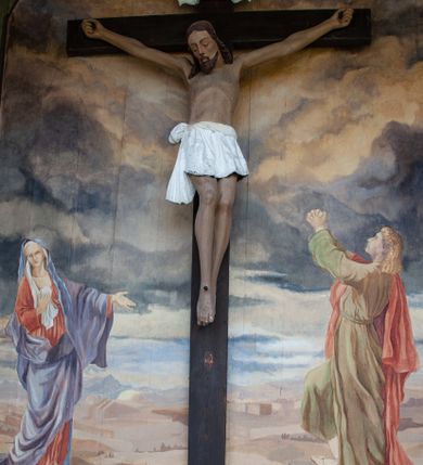 Zdjęcie nr 2: Figura Chrystusa umarłego, przybita jest do prostego krzyża trzema gwoździami. Ukazana została w lekkim zwisie ciała, o szeroko rozpostartych ramionach z zaciśniętymi dłońmi, nogi są delikatnie ugięte w kolanach, a stopy w układzie prawa na lewą. Twarz pociągła o wyraźnych rysach łuków brwiowych i prostego nosa, oczy są zamknięte. Okolona jest brodą oraz włosami opadającymi na ramiona. Ciało jest wychudzone, o delikatnym modelunku klatki piersiowej, z podkreślonymi mięśniami ramion wyłamanych z barków. Białe perizonium sięgające połowy ud, zawiązane jest na prawym biodrze ze zwisem tkaniny. Polichromia ciała naturalistyczna z delikatnie zaznaczonymi krwawiącymi ranami. 