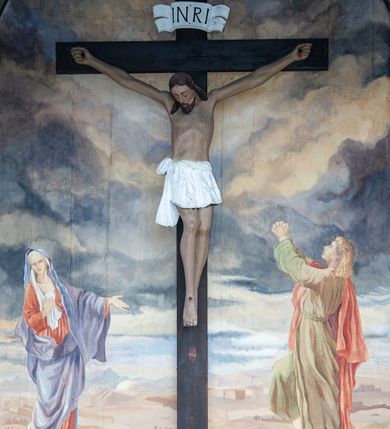 Zdjęcie nr 3: Figura Chrystusa umarłego, przybita jest do prostego krzyża trzema gwoździami. Ukazana została w lekkim zwisie ciała, o szeroko rozpostartych ramionach z zaciśniętymi dłońmi, nogi są delikatnie ugięte w kolanach, a stopy w układzie prawa na lewą. Twarz pociągła o wyraźnych rysach łuków brwiowych i prostego nosa, oczy są zamknięte. Okolona jest brodą oraz włosami opadającymi na ramiona. Ciało jest wychudzone, o delikatnym modelunku klatki piersiowej, z podkreślonymi mięśniami ramion wyłamanych z barków. Białe perizonium sięgające połowy ud, zawiązane jest na prawym biodrze ze zwisem tkaniny. Polichromia ciała naturalistyczna z delikatnie zaznaczonymi krwawiącymi ranami. 