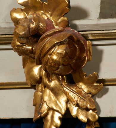 Zdjęcie nr 23: Ołtarz prostopadłościenny, murowany, w drewnianej obudowie, z drewnianą mensą. Antependium w kształcie leżącego prostokąta ujętego profilowaną ramą, dekorowane monogramem imienia MARIA w środku pola i symetrycznie rozłożonymi po bokach różanymi gałązkami. Na mensie ustawione architektoniczne tabernakulum. 
Nastawa w formie paludamentu podwiązanego po bokach sznurem z chwostami, lamowanego frędzlą, zwieńczonego baldachimem utworzonym z fragmentu wklęsło-wypukłego gzymsu z lambrekinem i rokokowym kartuszem. W polu paludamentu wnęka w kształcie stojącego prostokąta o wklęsłych górnych narożach w profilowanej ramie, ustawiona na cokole ujętym spływami wolutowymi. Wewnątrz obraz Matki Boskiej z Dzieciątkiem ujęty grubą ramą dekorowaną akantem i palmetami, ponad nim uskrzydlona główka anielska. Wnękę flankują dwa unoszące się putta, powyżej niej kartusz z monogramem Marii. Paludament dekorowany plastycznymi gwiazdami. Po bokach nastawy dwie bramki z otworami wejściowymi w formie stojącego prostokąta, zamkniętymi prostym gzymsem ze znajdującymi się powyżej postumentami dekorowanymi różami, na których stoją dwie figury aniołów. W górnej części, z obydwu stron nastawy poziome listwy konstrukcyjne mocujące całość retabulum do ścian bocznych prezbiterium, dekorowane są uskrzydlonymi główkami anielskimi z muszlami oraz roślinnymi festonami. Paludament polichromowany wewnątrz na biało, zewnątrz na niebiesko z pozłacanymi detalami.

