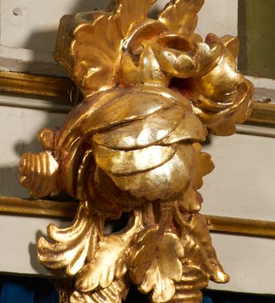 Zdjęcie nr 24: Ołtarz prostopadłościenny, murowany, w drewnianej obudowie, z drewnianą mensą. Antependium w kształcie leżącego prostokąta ujętego profilowaną ramą, dekorowane monogramem imienia MARIA w środku pola i symetrycznie rozłożonymi po bokach różanymi gałązkami. Na mensie ustawione architektoniczne tabernakulum. 
Nastawa w formie paludamentu podwiązanego po bokach sznurem z chwostami, lamowanego frędzlą, zwieńczonego baldachimem utworzonym z fragmentu wklęsło-wypukłego gzymsu z lambrekinem i rokokowym kartuszem. W polu paludamentu wnęka w kształcie stojącego prostokąta o wklęsłych górnych narożach w profilowanej ramie, ustawiona na cokole ujętym spływami wolutowymi. Wewnątrz obraz Matki Boskiej z Dzieciątkiem ujęty grubą ramą dekorowaną akantem i palmetami, ponad nim uskrzydlona główka anielska. Wnękę flankują dwa unoszące się putta, powyżej niej kartusz z monogramem Marii. Paludament dekorowany plastycznymi gwiazdami. Po bokach nastawy dwie bramki z otworami wejściowymi w formie stojącego prostokąta, zamkniętymi prostym gzymsem ze znajdującymi się powyżej postumentami dekorowanymi różami, na których stoją dwie figury aniołów. W górnej części, z obydwu stron nastawy poziome listwy konstrukcyjne mocujące całość retabulum do ścian bocznych prezbiterium, dekorowane są uskrzydlonymi główkami anielskimi z muszlami oraz roślinnymi festonami. Paludament polichromowany wewnątrz na biało, zewnątrz na niebiesko z pozłacanymi detalami.

