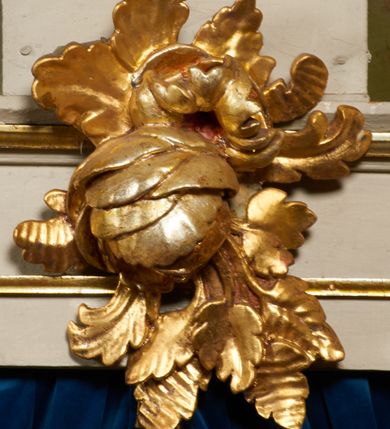 Zdjęcie nr 22: Ołtarz prostopadłościenny, murowany, w drewnianej obudowie, z drewnianą mensą. Antependium w kształcie leżącego prostokąta ujętego profilowaną ramą, dekorowane monogramem imienia MARIA w środku pola i symetrycznie rozłożonymi po bokach różanymi gałązkami. Na mensie ustawione architektoniczne tabernakulum. 
Nastawa w formie paludamentu podwiązanego po bokach sznurem z chwostami, lamowanego frędzlą, zwieńczonego baldachimem utworzonym z fragmentu wklęsło-wypukłego gzymsu z lambrekinem i rokokowym kartuszem. W polu paludamentu wnęka w kształcie stojącego prostokąta o wklęsłych górnych narożach w profilowanej ramie, ustawiona na cokole ujętym spływami wolutowymi. Wewnątrz obraz Matki Boskiej z Dzieciątkiem ujęty grubą ramą dekorowaną akantem i palmetami, ponad nim uskrzydlona główka anielska. Wnękę flankują dwa unoszące się putta, powyżej niej kartusz z monogramem Marii. Paludament dekorowany plastycznymi gwiazdami. Po bokach nastawy dwie bramki z otworami wejściowymi w formie stojącego prostokąta, zamkniętymi prostym gzymsem ze znajdującymi się powyżej postumentami dekorowanymi różami, na których stoją dwie figury aniołów. W górnej części, z obydwu stron nastawy poziome listwy konstrukcyjne mocujące całość retabulum do ścian bocznych prezbiterium, dekorowane są uskrzydlonymi główkami anielskimi z muszlami oraz roślinnymi festonami. Paludament polichromowany wewnątrz na biało, zewnątrz na niebiesko z pozłacanymi detalami.

