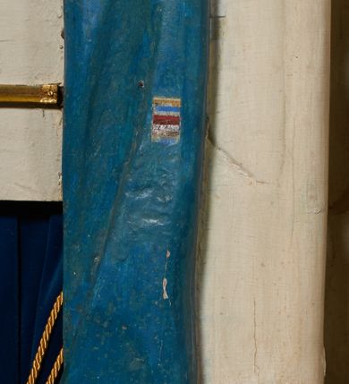 Zdjęcie nr 35: Ołtarz prostopadłościenny, murowany, w drewnianej obudowie, z drewnianą mensą. Antependium w kształcie leżącego prostokąta ujętego profilowaną ramą, dekorowane monogramem imienia MARIA w środku pola i symetrycznie rozłożonymi po bokach różanymi gałązkami. Na mensie ustawione architektoniczne tabernakulum. 
Nastawa w formie paludamentu podwiązanego po bokach sznurem z chwostami, lamowanego frędzlą, zwieńczonego baldachimem utworzonym z fragmentu wklęsło-wypukłego gzymsu z lambrekinem i rokokowym kartuszem. W polu paludamentu wnęka w kształcie stojącego prostokąta o wklęsłych górnych narożach w profilowanej ramie, ustawiona na cokole ujętym spływami wolutowymi. Wewnątrz obraz Matki Boskiej z Dzieciątkiem ujęty grubą ramą dekorowaną akantem i palmetami, ponad nim uskrzydlona główka anielska. Wnękę flankują dwa unoszące się putta, powyżej niej kartusz z monogramem Marii. Paludament dekorowany plastycznymi gwiazdami. Po bokach nastawy dwie bramki z otworami wejściowymi w formie stojącego prostokąta, zamkniętymi prostym gzymsem ze znajdującymi się powyżej postumentami dekorowanymi różami, na których stoją dwie figury aniołów. W górnej części, z obydwu stron nastawy poziome listwy konstrukcyjne mocujące całość retabulum do ścian bocznych prezbiterium, dekorowane są uskrzydlonymi główkami anielskimi z muszlami oraz roślinnymi festonami. Paludament polichromowany wewnątrz na biało, zewnątrz na niebiesko z pozłacanymi detalami.

