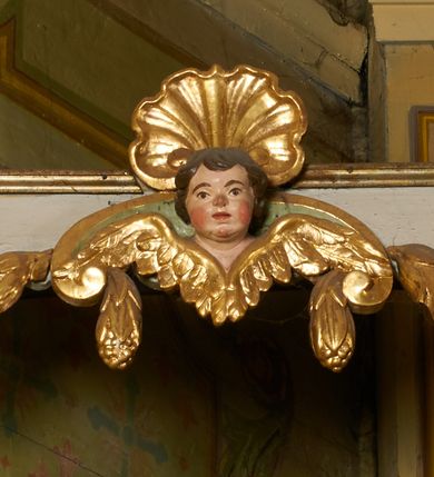 Zdjęcie nr 29: Ołtarz prostopadłościenny, murowany, w drewnianej obudowie, z drewnianą mensą. Antependium w kształcie leżącego prostokąta ujętego profilowaną ramą, dekorowane monogramem imienia MARIA w środku pola i symetrycznie rozłożonymi po bokach różanymi gałązkami. Na mensie ustawione architektoniczne tabernakulum. 
Nastawa w formie paludamentu podwiązanego po bokach sznurem z chwostami, lamowanego frędzlą, zwieńczonego baldachimem utworzonym z fragmentu wklęsło-wypukłego gzymsu z lambrekinem i rokokowym kartuszem. W polu paludamentu wnęka w kształcie stojącego prostokąta o wklęsłych górnych narożach w profilowanej ramie, ustawiona na cokole ujętym spływami wolutowymi. Wewnątrz obraz Matki Boskiej z Dzieciątkiem ujęty grubą ramą dekorowaną akantem i palmetami, ponad nim uskrzydlona główka anielska. Wnękę flankują dwa unoszące się putta, powyżej niej kartusz z monogramem Marii. Paludament dekorowany plastycznymi gwiazdami. Po bokach nastawy dwie bramki z otworami wejściowymi w formie stojącego prostokąta, zamkniętymi prostym gzymsem ze znajdującymi się powyżej postumentami dekorowanymi różami, na których stoją dwie figury aniołów. W górnej części, z obydwu stron nastawy poziome listwy konstrukcyjne mocujące całość retabulum do ścian bocznych prezbiterium, dekorowane są uskrzydlonymi główkami anielskimi z muszlami oraz roślinnymi festonami. Paludament polichromowany wewnątrz na biało, zewnątrz na niebiesko z pozłacanymi detalami.

