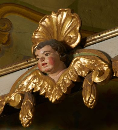 Zdjęcie nr 32: Ołtarz prostopadłościenny, murowany, w drewnianej obudowie, z drewnianą mensą. Antependium w kształcie leżącego prostokąta ujętego profilowaną ramą, dekorowane monogramem imienia MARIA w środku pola i symetrycznie rozłożonymi po bokach różanymi gałązkami. Na mensie ustawione architektoniczne tabernakulum. 
Nastawa w formie paludamentu podwiązanego po bokach sznurem z chwostami, lamowanego frędzlą, zwieńczonego baldachimem utworzonym z fragmentu wklęsło-wypukłego gzymsu z lambrekinem i rokokowym kartuszem. W polu paludamentu wnęka w kształcie stojącego prostokąta o wklęsłych górnych narożach w profilowanej ramie, ustawiona na cokole ujętym spływami wolutowymi. Wewnątrz obraz Matki Boskiej z Dzieciątkiem ujęty grubą ramą dekorowaną akantem i palmetami, ponad nim uskrzydlona główka anielska. Wnękę flankują dwa unoszące się putta, powyżej niej kartusz z monogramem Marii. Paludament dekorowany plastycznymi gwiazdami. Po bokach nastawy dwie bramki z otworami wejściowymi w formie stojącego prostokąta, zamkniętymi prostym gzymsem ze znajdującymi się powyżej postumentami dekorowanymi różami, na których stoją dwie figury aniołów. W górnej części, z obydwu stron nastawy poziome listwy konstrukcyjne mocujące całość retabulum do ścian bocznych prezbiterium, dekorowane są uskrzydlonymi główkami anielskimi z muszlami oraz roślinnymi festonami. Paludament polichromowany wewnątrz na biało, zewnątrz na niebiesko z pozłacanymi detalami.

