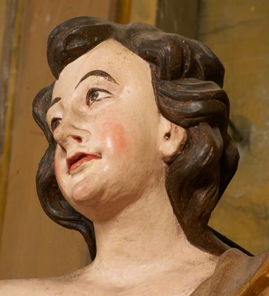 Zdjęcie nr 51: Ołtarz prostopadłościenny, murowany, w drewnianej obudowie, z drewnianą mensą. Antependium w kształcie leżącego prostokąta ujętego profilowaną ramą, dekorowane monogramem imienia MARIA w środku pola i symetrycznie rozłożonymi po bokach różanymi gałązkami. Na mensie ustawione architektoniczne tabernakulum. 
Nastawa w formie paludamentu podwiązanego po bokach sznurem z chwostami, lamowanego frędzlą, zwieńczonego baldachimem utworzonym z fragmentu wklęsło-wypukłego gzymsu z lambrekinem i rokokowym kartuszem. W polu paludamentu wnęka w kształcie stojącego prostokąta o wklęsłych górnych narożach w profilowanej ramie, ustawiona na cokole ujętym spływami wolutowymi. Wewnątrz obraz Matki Boskiej z Dzieciątkiem ujęty grubą ramą dekorowaną akantem i palmetami, ponad nim uskrzydlona główka anielska. Wnękę flankują dwa unoszące się putta, powyżej niej kartusz z monogramem Marii. Paludament dekorowany plastycznymi gwiazdami. Po bokach nastawy dwie bramki z otworami wejściowymi w formie stojącego prostokąta, zamkniętymi prostym gzymsem ze znajdującymi się powyżej postumentami dekorowanymi różami, na których stoją dwie figury aniołów. W górnej części, z obydwu stron nastawy poziome listwy konstrukcyjne mocujące całość retabulum do ścian bocznych prezbiterium, dekorowane są uskrzydlonymi główkami anielskimi z muszlami oraz roślinnymi festonami. Paludament polichromowany wewnątrz na biało, zewnątrz na niebiesko z pozłacanymi detalami.

