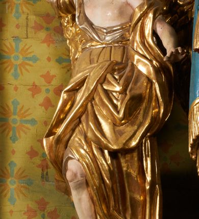 Zdjęcie nr 64: Ołtarz prostopadłościenny, murowany, w drewnianej obudowie, z drewnianą mensą. Antependium w kształcie leżącego prostokąta ujętego profilowaną ramą, dekorowane monogramem imienia MARIA w środku pola i symetrycznie rozłożonymi po bokach różanymi gałązkami. Na mensie ustawione architektoniczne tabernakulum. 
Nastawa w formie paludamentu podwiązanego po bokach sznurem z chwostami, lamowanego frędzlą, zwieńczonego baldachimem utworzonym z fragmentu wklęsło-wypukłego gzymsu z lambrekinem i rokokowym kartuszem. W polu paludamentu wnęka w kształcie stojącego prostokąta o wklęsłych górnych narożach w profilowanej ramie, ustawiona na cokole ujętym spływami wolutowymi. Wewnątrz obraz Matki Boskiej z Dzieciątkiem ujęty grubą ramą dekorowaną akantem i palmetami, ponad nim uskrzydlona główka anielska. Wnękę flankują dwa unoszące się putta, powyżej niej kartusz z monogramem Marii. Paludament dekorowany plastycznymi gwiazdami. Po bokach nastawy dwie bramki z otworami wejściowymi w formie stojącego prostokąta, zamkniętymi prostym gzymsem ze znajdującymi się powyżej postumentami dekorowanymi różami, na których stoją dwie figury aniołów. W górnej części, z obydwu stron nastawy poziome listwy konstrukcyjne mocujące całość retabulum do ścian bocznych prezbiterium, dekorowane są uskrzydlonymi główkami anielskimi z muszlami oraz roślinnymi festonami. Paludament polichromowany wewnątrz na biało, zewnątrz na niebiesko z pozłacanymi detalami.

