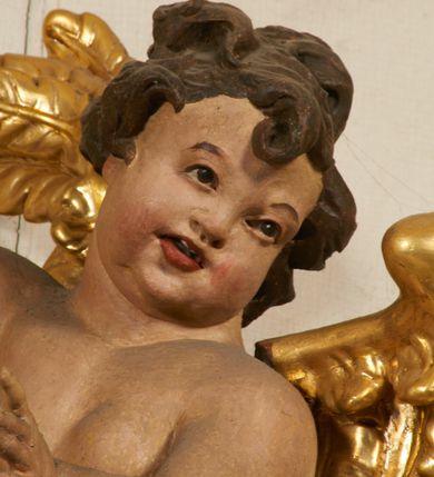 Zdjęcie nr 88: Ołtarz prostopadłościenny, murowany, w drewnianej obudowie, z drewnianą mensą. Antependium w kształcie leżącego prostokąta ujętego profilowaną ramą, dekorowane monogramem imienia MARIA w środku pola i symetrycznie rozłożonymi po bokach różanymi gałązkami. Na mensie ustawione architektoniczne tabernakulum. 
Nastawa w formie paludamentu podwiązanego po bokach sznurem z chwostami, lamowanego frędzlą, zwieńczonego baldachimem utworzonym z fragmentu wklęsło-wypukłego gzymsu z lambrekinem i rokokowym kartuszem. W polu paludamentu wnęka w kształcie stojącego prostokąta o wklęsłych górnych narożach w profilowanej ramie, ustawiona na cokole ujętym spływami wolutowymi. Wewnątrz obraz Matki Boskiej z Dzieciątkiem ujęty grubą ramą dekorowaną akantem i palmetami, ponad nim uskrzydlona główka anielska. Wnękę flankują dwa unoszące się putta, powyżej niej kartusz z monogramem Marii. Paludament dekorowany plastycznymi gwiazdami. Po bokach nastawy dwie bramki z otworami wejściowymi w formie stojącego prostokąta, zamkniętymi prostym gzymsem ze znajdującymi się powyżej postumentami dekorowanymi różami, na których stoją dwie figury aniołów. W górnej części, z obydwu stron nastawy poziome listwy konstrukcyjne mocujące całość retabulum do ścian bocznych prezbiterium, dekorowane są uskrzydlonymi główkami anielskimi z muszlami oraz roślinnymi festonami. Paludament polichromowany wewnątrz na biało, zewnątrz na niebiesko z pozłacanymi detalami.


