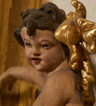 Zdjęcie nr 89: Ołtarz prostopadłościenny, murowany, w drewnianej obudowie, z drewnianą mensą. Antependium w kształcie leżącego prostokąta ujętego profilowaną ramą, dekorowane monogramem imienia MARIA w środku pola i symetrycznie rozłożonymi po bokach różanymi gałązkami. Na mensie ustawione architektoniczne tabernakulum. 
Nastawa w formie paludamentu podwiązanego po bokach sznurem z chwostami, lamowanego frędzlą, zwieńczonego baldachimem utworzonym z fragmentu wklęsło-wypukłego gzymsu z lambrekinem i rokokowym kartuszem. W polu paludamentu wnęka w kształcie stojącego prostokąta o wklęsłych górnych narożach w profilowanej ramie, ustawiona na cokole ujętym spływami wolutowymi. Wewnątrz obraz Matki Boskiej z Dzieciątkiem ujęty grubą ramą dekorowaną akantem i palmetami, ponad nim uskrzydlona główka anielska. Wnękę flankują dwa unoszące się putta, powyżej niej kartusz z monogramem Marii. Paludament dekorowany plastycznymi gwiazdami. Po bokach nastawy dwie bramki z otworami wejściowymi w formie stojącego prostokąta, zamkniętymi prostym gzymsem ze znajdującymi się powyżej postumentami dekorowanymi różami, na których stoją dwie figury aniołów. W górnej części, z obydwu stron nastawy poziome listwy konstrukcyjne mocujące całość retabulum do ścian bocznych prezbiterium, dekorowane są uskrzydlonymi główkami anielskimi z muszlami oraz roślinnymi festonami. Paludament polichromowany wewnątrz na biało, zewnątrz na niebiesko z pozłacanymi detalami.

