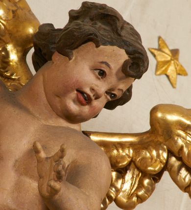 Zdjęcie nr 91: Ołtarz prostopadłościenny, murowany, w drewnianej obudowie, z drewnianą mensą. Antependium w kształcie leżącego prostokąta ujętego profilowaną ramą, dekorowane monogramem imienia MARIA w środku pola i symetrycznie rozłożonymi po bokach różanymi gałązkami. Na mensie ustawione architektoniczne tabernakulum. 
Nastawa w formie paludamentu podwiązanego po bokach sznurem z chwostami, lamowanego frędzlą, zwieńczonego baldachimem utworzonym z fragmentu wklęsło-wypukłego gzymsu z lambrekinem i rokokowym kartuszem. W polu paludamentu wnęka w kształcie stojącego prostokąta o wklęsłych górnych narożach w profilowanej ramie, ustawiona na cokole ujętym spływami wolutowymi. Wewnątrz obraz Matki Boskiej z Dzieciątkiem ujęty grubą ramą dekorowaną akantem i palmetami, ponad nim uskrzydlona główka anielska. Wnękę flankują dwa unoszące się putta, powyżej niej kartusz z monogramem Marii. Paludament dekorowany plastycznymi gwiazdami. Po bokach nastawy dwie bramki z otworami wejściowymi w formie stojącego prostokąta, zamkniętymi prostym gzymsem ze znajdującymi się powyżej postumentami dekorowanymi różami, na których stoją dwie figury aniołów. W górnej części, z obydwu stron nastawy poziome listwy konstrukcyjne mocujące całość retabulum do ścian bocznych prezbiterium, dekorowane są uskrzydlonymi główkami anielskimi z muszlami oraz roślinnymi festonami. Paludament polichromowany wewnątrz na biało, zewnątrz na niebiesko z pozłacanymi detalami.

