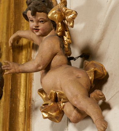 Zdjęcie nr 86: Ołtarz prostopadłościenny, murowany, w drewnianej obudowie, z drewnianą mensą. Antependium w kształcie leżącego prostokąta ujętego profilowaną ramą, dekorowane monogramem imienia MARIA w środku pola i symetrycznie rozłożonymi po bokach różanymi gałązkami. Na mensie ustawione architektoniczne tabernakulum. 
Nastawa w formie paludamentu podwiązanego po bokach sznurem z chwostami, lamowanego frędzlą, zwieńczonego baldachimem utworzonym z fragmentu wklęsło-wypukłego gzymsu z lambrekinem i rokokowym kartuszem. W polu paludamentu wnęka w kształcie stojącego prostokąta o wklęsłych górnych narożach w profilowanej ramie, ustawiona na cokole ujętym spływami wolutowymi. Wewnątrz obraz Matki Boskiej z Dzieciątkiem ujęty grubą ramą dekorowaną akantem i palmetami, ponad nim uskrzydlona główka anielska. Wnękę flankują dwa unoszące się putta, powyżej niej kartusz z monogramem Marii. Paludament dekorowany plastycznymi gwiazdami. Po bokach nastawy dwie bramki z otworami wejściowymi w formie stojącego prostokąta, zamkniętymi prostym gzymsem ze znajdującymi się powyżej postumentami dekorowanymi różami, na których stoją dwie figury aniołów. W górnej części, z obydwu stron nastawy poziome listwy konstrukcyjne mocujące całość retabulum do ścian bocznych prezbiterium, dekorowane są uskrzydlonymi główkami anielskimi z muszlami oraz roślinnymi festonami. Paludament polichromowany wewnątrz na biało, zewnątrz na niebiesko z pozłacanymi detalami.

