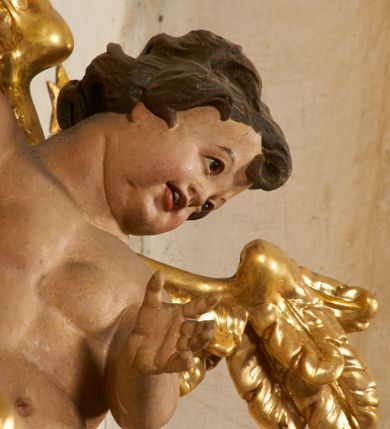 Zdjęcie nr 90: Ołtarz prostopadłościenny, murowany, w drewnianej obudowie, z drewnianą mensą. Antependium w kształcie leżącego prostokąta ujętego profilowaną ramą, dekorowane monogramem imienia MARIA w środku pola i symetrycznie rozłożonymi po bokach różanymi gałązkami. Na mensie ustawione architektoniczne tabernakulum. 
Nastawa w formie paludamentu podwiązanego po bokach sznurem z chwostami, lamowanego frędzlą, zwieńczonego baldachimem utworzonym z fragmentu wklęsło-wypukłego gzymsu z lambrekinem i rokokowym kartuszem. W polu paludamentu wnęka w kształcie stojącego prostokąta o wklęsłych górnych narożach w profilowanej ramie, ustawiona na cokole ujętym spływami wolutowymi. Wewnątrz obraz Matki Boskiej z Dzieciątkiem ujęty grubą ramą dekorowaną akantem i palmetami, ponad nim uskrzydlona główka anielska. Wnękę flankują dwa unoszące się putta, powyżej niej kartusz z monogramem Marii. Paludament dekorowany plastycznymi gwiazdami. Po bokach nastawy dwie bramki z otworami wejściowymi w formie stojącego prostokąta, zamkniętymi prostym gzymsem ze znajdującymi się powyżej postumentami dekorowanymi różami, na których stoją dwie figury aniołów. W górnej części, z obydwu stron nastawy poziome listwy konstrukcyjne mocujące całość retabulum do ścian bocznych prezbiterium, dekorowane są uskrzydlonymi główkami anielskimi z muszlami oraz roślinnymi festonami. Paludament polichromowany wewnątrz na biało, zewnątrz na niebiesko z pozłacanymi detalami.

