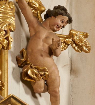 Zdjęcie nr 87: Ołtarz prostopadłościenny, murowany, w drewnianej obudowie, z drewnianą mensą. Antependium w kształcie leżącego prostokąta ujętego profilowaną ramą, dekorowane monogramem imienia MARIA w środku pola i symetrycznie rozłożonymi po bokach różanymi gałązkami. Na mensie ustawione architektoniczne tabernakulum. 
Nastawa w formie paludamentu podwiązanego po bokach sznurem z chwostami, lamowanego frędzlą, zwieńczonego baldachimem utworzonym z fragmentu wklęsło-wypukłego gzymsu z lambrekinem i rokokowym kartuszem. W polu paludamentu wnęka w kształcie stojącego prostokąta o wklęsłych górnych narożach w profilowanej ramie, ustawiona na cokole ujętym spływami wolutowymi. Wewnątrz obraz Matki Boskiej z Dzieciątkiem ujęty grubą ramą dekorowaną akantem i palmetami, ponad nim uskrzydlona główka anielska. Wnękę flankują dwa unoszące się putta, powyżej niej kartusz z monogramem Marii. Paludament dekorowany plastycznymi gwiazdami. Po bokach nastawy dwie bramki z otworami wejściowymi w formie stojącego prostokąta, zamkniętymi prostym gzymsem ze znajdującymi się powyżej postumentami dekorowanymi różami, na których stoją dwie figury aniołów. W górnej części, z obydwu stron nastawy poziome listwy konstrukcyjne mocujące całość retabulum do ścian bocznych prezbiterium, dekorowane są uskrzydlonymi główkami anielskimi z muszlami oraz roślinnymi festonami. Paludament polichromowany wewnątrz na biało, zewnątrz na niebiesko z pozłacanymi detalami.

