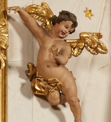 Zdjęcie nr 83: Ołtarz prostopadłościenny, murowany, w drewnianej obudowie, z drewnianą mensą. Antependium w kształcie leżącego prostokąta ujętego profilowaną ramą, dekorowane monogramem imienia MARIA w środku pola i symetrycznie rozłożonymi po bokach różanymi gałązkami. Na mensie ustawione architektoniczne tabernakulum. 
Nastawa w formie paludamentu podwiązanego po bokach sznurem z chwostami, lamowanego frędzlą, zwieńczonego baldachimem utworzonym z fragmentu wklęsło-wypukłego gzymsu z lambrekinem i rokokowym kartuszem. W polu paludamentu wnęka w kształcie stojącego prostokąta o wklęsłych górnych narożach w profilowanej ramie, ustawiona na cokole ujętym spływami wolutowymi. Wewnątrz obraz Matki Boskiej z Dzieciątkiem ujęty grubą ramą dekorowaną akantem i palmetami, ponad nim uskrzydlona główka anielska. Wnękę flankują dwa unoszące się putta, powyżej niej kartusz z monogramem Marii. Paludament dekorowany plastycznymi gwiazdami. Po bokach nastawy dwie bramki z otworami wejściowymi w formie stojącego prostokąta, zamkniętymi prostym gzymsem ze znajdującymi się powyżej postumentami dekorowanymi różami, na których stoją dwie figury aniołów. W górnej części, z obydwu stron nastawy poziome listwy konstrukcyjne mocujące całość retabulum do ścian bocznych prezbiterium, dekorowane są uskrzydlonymi główkami anielskimi z muszlami oraz roślinnymi festonami. Paludament polichromowany wewnątrz na biało, zewnątrz na niebiesko z pozłacanymi detalami.

