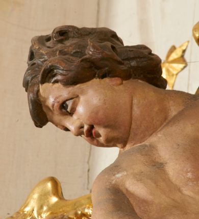 Zdjęcie nr 99: Ołtarz prostopadłościenny, murowany, w drewnianej obudowie, z drewnianą mensą. Antependium w kształcie leżącego prostokąta ujętego profilowaną ramą, dekorowane monogramem imienia MARIA w środku pola i symetrycznie rozłożonymi po bokach różanymi gałązkami. Na mensie ustawione architektoniczne tabernakulum. 
Nastawa w formie paludamentu podwiązanego po bokach sznurem z chwostami, lamowanego frędzlą, zwieńczonego baldachimem utworzonym z fragmentu wklęsło-wypukłego gzymsu z lambrekinem i rokokowym kartuszem. W polu paludamentu wnęka w kształcie stojącego prostokąta o wklęsłych górnych narożach w profilowanej ramie, ustawiona na cokole ujętym spływami wolutowymi. Wewnątrz obraz Matki Boskiej z Dzieciątkiem ujęty grubą ramą dekorowaną akantem i palmetami, ponad nim uskrzydlona główka anielska. Wnękę flankują dwa unoszące się putta, powyżej niej kartusz z monogramem Marii. Paludament dekorowany plastycznymi gwiazdami. Po bokach nastawy dwie bramki z otworami wejściowymi w formie stojącego prostokąta, zamkniętymi prostym gzymsem ze znajdującymi się powyżej postumentami dekorowanymi różami, na których stoją dwie figury aniołów. W górnej części, z obydwu stron nastawy poziome listwy konstrukcyjne mocujące całość retabulum do ścian bocznych prezbiterium, dekorowane są uskrzydlonymi główkami anielskimi z muszlami oraz roślinnymi festonami. Paludament polichromowany wewnątrz na biało, zewnątrz na niebiesko z pozłacanymi detalami.

