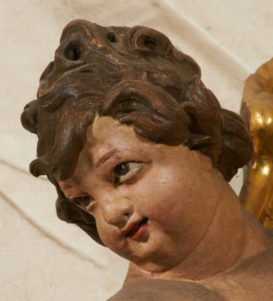 Zdjęcie nr 100: Ołtarz prostopadłościenny, murowany, w drewnianej obudowie, z drewnianą mensą. Antependium w kształcie leżącego prostokąta ujętego profilowaną ramą, dekorowane monogramem imienia MARIA w środku pola i symetrycznie rozłożonymi po bokach różanymi gałązkami. Na mensie ustawione architektoniczne tabernakulum. 
Nastawa w formie paludamentu podwiązanego po bokach sznurem z chwostami, lamowanego frędzlą, zwieńczonego baldachimem utworzonym z fragmentu wklęsło-wypukłego gzymsu z lambrekinem i rokokowym kartuszem. W polu paludamentu wnęka w kształcie stojącego prostokąta o wklęsłych górnych narożach w profilowanej ramie, ustawiona na cokole ujętym spływami wolutowymi. Wewnątrz obraz Matki Boskiej z Dzieciątkiem ujęty grubą ramą dekorowaną akantem i palmetami, ponad nim uskrzydlona główka anielska. Wnękę flankują dwa unoszące się putta, powyżej niej kartusz z monogramem Marii. Paludament dekorowany plastycznymi gwiazdami. Po bokach nastawy dwie bramki z otworami wejściowymi w formie stojącego prostokąta, zamkniętymi prostym gzymsem ze znajdującymi się powyżej postumentami dekorowanymi różami, na których stoją dwie figury aniołów. W górnej części, z obydwu stron nastawy poziome listwy konstrukcyjne mocujące całość retabulum do ścian bocznych prezbiterium, dekorowane są uskrzydlonymi główkami anielskimi z muszlami oraz roślinnymi festonami. Paludament polichromowany wewnątrz na biało, zewnątrz na niebiesko z pozłacanymi detalami.

