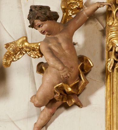 Zdjęcie nr 92: Ołtarz prostopadłościenny, murowany, w drewnianej obudowie, z drewnianą mensą. Antependium w kształcie leżącego prostokąta ujętego profilowaną ramą, dekorowane monogramem imienia MARIA w środku pola i symetrycznie rozłożonymi po bokach różanymi gałązkami. Na mensie ustawione architektoniczne tabernakulum. 
Nastawa w formie paludamentu podwiązanego po bokach sznurem z chwostami, lamowanego frędzlą, zwieńczonego baldachimem utworzonym z fragmentu wklęsło-wypukłego gzymsu z lambrekinem i rokokowym kartuszem. W polu paludamentu wnęka w kształcie stojącego prostokąta o wklęsłych górnych narożach w profilowanej ramie, ustawiona na cokole ujętym spływami wolutowymi. Wewnątrz obraz Matki Boskiej z Dzieciątkiem ujęty grubą ramą dekorowaną akantem i palmetami, ponad nim uskrzydlona główka anielska. Wnękę flankują dwa unoszące się putta, powyżej niej kartusz z monogramem Marii. Paludament dekorowany plastycznymi gwiazdami. Po bokach nastawy dwie bramki z otworami wejściowymi w formie stojącego prostokąta, zamkniętymi prostym gzymsem ze znajdującymi się powyżej postumentami dekorowanymi różami, na których stoją dwie figury aniołów. W górnej części, z obydwu stron nastawy poziome listwy konstrukcyjne mocujące całość retabulum do ścian bocznych prezbiterium, dekorowane są uskrzydlonymi główkami anielskimi z muszlami oraz roślinnymi festonami. Paludament polichromowany wewnątrz na biało, zewnątrz na niebiesko z pozłacanymi detalami.

