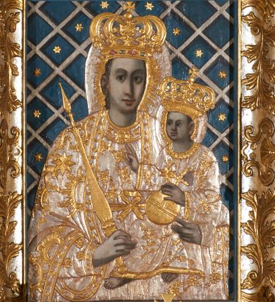 Zdjęcie nr 1: Obraz w kształcie pionowego prostokąta, z przedstawieniem Matki Boskiej z Dzieciątkiem, na niebieskim tle dekorowanym srebrzoną kratką, z malowanymi na drewnie partiami twarzy, dłoni i stóp oraz partiami szat i insygniami zasłoniętymi przez sukienki. Matka Boska ukazana w półpostaci, zwrócona delikatnie w trzech czwartych w lewą stronę, na lewym przedramieniu podtrzymuje Dzieciątko, a w prawej dłoni trzyma berło. Twarz pociągła, owalna, o dużych oczach, prostym, długim nosie i pełnych ustach, z odsłoniętym dużym prawym uchem. Łagodne rysy wydobyte zostały ostrym kontrastem światłocienia. Na głowie ma koronę zamkniętą, wokół głowy glorię promienistą i nimb zamknięty. Ubrana jest w suknię, dekorowaną gałązkami kwiatowymi, przepasaną w talii wstążką oraz płaszcz narzucony na ramiona, z ośmioramienną gwiazdą na prawym ramieniu, dekorowany ornamentem rocaille&#039;owym z ośmioramienną gwiazdą na prawym ramieniu. Dzieciątko w pozycji siedzącej, zwrócone jest w trzech czwartych w prawą stronę, prawą dłonią błogosławi, lewą przytrzymuje na kolanie jabłko królewskie. Jego twarz jest okrągła o rysach wydobytych silnym światłocieniem, o dużych oczach, niewielkim nosie i pełnych ustach z odsłoniętym lewym, dużym uchem. Na głowie ma koronę zamkniętą, wokół twarzy glorię promienistą oraz nimb zamknięty. Ubrane jest w tunikę dekorowaną gałązkami kwiatowymi i lamówką. Obraz ujęty posrebrzaną ramą z plastycznym, rokokowym i pozłacanym ornamentem. 