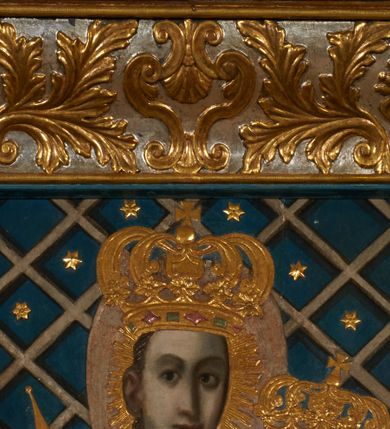 Zdjęcie nr 22: Obraz w kształcie pionowego prostokąta, z przedstawieniem Matki Boskiej z Dzieciątkiem, na niebieskim tle dekorowanym srebrzoną kratką, z malowanymi na drewnie partiami twarzy, dłoni i stóp oraz partiami szat i insygniami zasłoniętymi przez sukienki. Matka Boska ukazana w półpostaci, zwrócona delikatnie w trzech czwartych w lewą stronę, na lewym przedramieniu podtrzymuje Dzieciątko, a w prawej dłoni trzyma berło. Twarz pociągła, owalna, o dużych oczach, prostym, długim nosie i pełnych ustach, z odsłoniętym dużym prawym uchem. Łagodne rysy wydobyte zostały ostrym kontrastem światłocienia. Na głowie ma koronę zamkniętą, wokół głowy glorię promienistą i nimb zamknięty. Ubrana jest w suknię, dekorowaną gałązkami kwiatowymi, przepasaną w talii wstążką oraz płaszcz narzucony na ramiona, z ośmioramienną gwiazdą na prawym ramieniu, dekorowany ornamentem rocaille'owym z ośmioramienną gwiazdą na prawym ramieniu. Dzieciątko w pozycji siedzącej, zwrócone jest w trzech czwartych w prawą stronę, prawą dłonią błogosławi, lewą przytrzymuje na kolanie jabłko królewskie. Jego twarz jest okrągła o rysach wydobytych silnym światłocieniem, o dużych oczach, niewielkim nosie i pełnych ustach z odsłoniętym lewym, dużym uchem. Na głowie ma koronę zamkniętą, wokół twarzy glorię promienistą oraz nimb zamknięty. Ubrane jest w tunikę dekorowaną gałązkami kwiatowymi i lamówką. Obraz ujęty posrebrzaną ramą z plastycznym, rokokowym i pozłacanym ornamentem. 