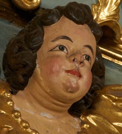 Zdjęcie nr 8: Obraz w kształcie pionowego prostokąta, z przedstawieniem Matki Boskiej z Dzieciątkiem, na niebieskim tle dekorowanym srebrzoną kratką, z malowanymi na drewnie partiami twarzy, dłoni i stóp oraz partiami szat i insygniami zasłoniętymi przez sukienki. Matka Boska ukazana w półpostaci, zwrócona delikatnie w trzech czwartych w lewą stronę, na lewym przedramieniu podtrzymuje Dzieciątko, a w prawej dłoni trzyma berło. Twarz pociągła, owalna, o dużych oczach, prostym, długim nosie i pełnych ustach, z odsłoniętym dużym prawym uchem. Łagodne rysy wydobyte zostały ostrym kontrastem światłocienia. Na głowie ma koronę zamkniętą, wokół głowy glorię promienistą i nimb zamknięty. Ubrana jest w suknię, dekorowaną gałązkami kwiatowymi, przepasaną w talii wstążką oraz płaszcz narzucony na ramiona, z ośmioramienną gwiazdą na prawym ramieniu, dekorowany ornamentem rocaille&#039;owym z ośmioramienną gwiazdą na prawym ramieniu. Dzieciątko w pozycji siedzącej, zwrócone jest w trzech czwartych w prawą stronę, prawą dłonią błogosławi, lewą przytrzymuje na kolanie jabłko królewskie. Jego twarz jest okrągła o rysach wydobytych silnym światłocieniem, o dużych oczach, niewielkim nosie i pełnych ustach z odsłoniętym lewym, dużym uchem. Na głowie ma koronę zamkniętą, wokół twarzy glorię promienistą oraz nimb zamknięty. Ubrane jest w tunikę dekorowaną gałązkami kwiatowymi i lamówką. Obraz ujęty posrebrzaną ramą z plastycznym, rokokowym i pozłacanym ornamentem. 