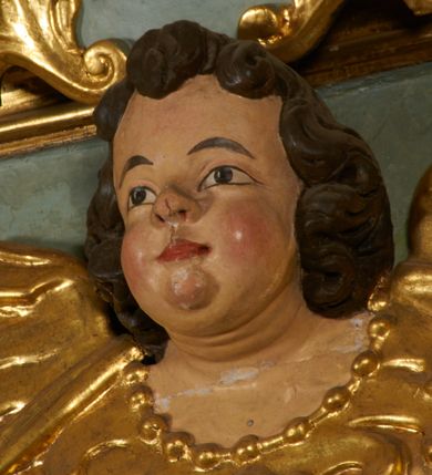 Zdjęcie nr 7: Obraz w kształcie pionowego prostokąta, z przedstawieniem Matki Boskiej z Dzieciątkiem, na niebieskim tle dekorowanym srebrzoną kratką, z malowanymi na drewnie partiami twarzy, dłoni i stóp oraz partiami szat i insygniami zasłoniętymi przez sukienki. Matka Boska ukazana w półpostaci, zwrócona delikatnie w trzech czwartych w lewą stronę, na lewym przedramieniu podtrzymuje Dzieciątko, a w prawej dłoni trzyma berło. Twarz pociągła, owalna, o dużych oczach, prostym, długim nosie i pełnych ustach, z odsłoniętym dużym prawym uchem. Łagodne rysy wydobyte zostały ostrym kontrastem światłocienia. Na głowie ma koronę zamkniętą, wokół głowy glorię promienistą i nimb zamknięty. Ubrana jest w suknię, dekorowaną gałązkami kwiatowymi, przepasaną w talii wstążką oraz płaszcz narzucony na ramiona, z ośmioramienną gwiazdą na prawym ramieniu, dekorowany ornamentem rocaille&#039;owym z ośmioramienną gwiazdą na prawym ramieniu. Dzieciątko w pozycji siedzącej, zwrócone jest w trzech czwartych w prawą stronę, prawą dłonią błogosławi, lewą przytrzymuje na kolanie jabłko królewskie. Jego twarz jest okrągła o rysach wydobytych silnym światłocieniem, o dużych oczach, niewielkim nosie i pełnych ustach z odsłoniętym lewym, dużym uchem. Na głowie ma koronę zamkniętą, wokół twarzy glorię promienistą oraz nimb zamknięty. Ubrane jest w tunikę dekorowaną gałązkami kwiatowymi i lamówką. Obraz ujęty posrebrzaną ramą z plastycznym, rokokowym i pozłacanym ornamentem. 