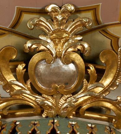 Zdjęcie nr 14: Obraz w kształcie pionowego prostokąta, z przedstawieniem Matki Boskiej z Dzieciątkiem, na niebieskim tle dekorowanym srebrzoną kratką, z malowanymi na drewnie partiami twarzy, dłoni i stóp oraz partiami szat i insygniami zasłoniętymi przez sukienki. Matka Boska ukazana w półpostaci, zwrócona delikatnie w trzech czwartych w lewą stronę, na lewym przedramieniu podtrzymuje Dzieciątko, a w prawej dłoni trzyma berło. Twarz pociągła, owalna, o dużych oczach, prostym, długim nosie i pełnych ustach, z odsłoniętym dużym prawym uchem. Łagodne rysy wydobyte zostały ostrym kontrastem światłocienia. Na głowie ma koronę zamkniętą, wokół głowy glorię promienistą i nimb zamknięty. Ubrana jest w suknię, dekorowaną gałązkami kwiatowymi, przepasaną w talii wstążką oraz płaszcz narzucony na ramiona, z ośmioramienną gwiazdą na prawym ramieniu, dekorowany ornamentem rocaille'owym z ośmioramienną gwiazdą na prawym ramieniu. Dzieciątko w pozycji siedzącej, zwrócone jest w trzech czwartych w prawą stronę, prawą dłonią błogosławi, lewą przytrzymuje na kolanie jabłko królewskie. Jego twarz jest okrągła o rysach wydobytych silnym światłocieniem, o dużych oczach, niewielkim nosie i pełnych ustach z odsłoniętym lewym, dużym uchem. Na głowie ma koronę zamkniętą, wokół twarzy glorię promienistą oraz nimb zamknięty. Ubrane jest w tunikę dekorowaną gałązkami kwiatowymi i lamówką. Obraz ujęty posrebrzaną ramą z plastycznym, rokokowym i pozłacanym ornamentem. 