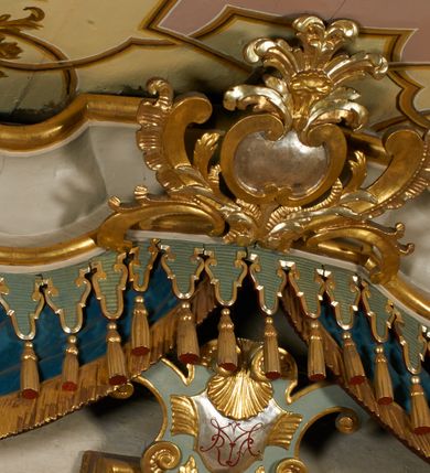 Zdjęcie nr 10: Obraz w kształcie pionowego prostokąta, z przedstawieniem Matki Boskiej z Dzieciątkiem, na niebieskim tle dekorowanym srebrzoną kratką, z malowanymi na drewnie partiami twarzy, dłoni i stóp oraz partiami szat i insygniami zasłoniętymi przez sukienki. Matka Boska ukazana w półpostaci, zwrócona delikatnie w trzech czwartych w lewą stronę, na lewym przedramieniu podtrzymuje Dzieciątko, a w prawej dłoni trzyma berło. Twarz pociągła, owalna, o dużych oczach, prostym, długim nosie i pełnych ustach, z odsłoniętym dużym prawym uchem. Łagodne rysy wydobyte zostały ostrym kontrastem światłocienia. Na głowie ma koronę zamkniętą, wokół głowy glorię promienistą i nimb zamknięty. Ubrana jest w suknię, dekorowaną gałązkami kwiatowymi, przepasaną w talii wstążką oraz płaszcz narzucony na ramiona, z ośmioramienną gwiazdą na prawym ramieniu, dekorowany ornamentem rocaille'owym z ośmioramienną gwiazdą na prawym ramieniu. Dzieciątko w pozycji siedzącej, zwrócone jest w trzech czwartych w prawą stronę, prawą dłonią błogosławi, lewą przytrzymuje na kolanie jabłko królewskie. Jego twarz jest okrągła o rysach wydobytych silnym światłocieniem, o dużych oczach, niewielkim nosie i pełnych ustach z odsłoniętym lewym, dużym uchem. Na głowie ma koronę zamkniętą, wokół twarzy glorię promienistą oraz nimb zamknięty. Ubrane jest w tunikę dekorowaną gałązkami kwiatowymi i lamówką. Obraz ujęty posrebrzaną ramą z plastycznym, rokokowym i pozłacanym ornamentem. 