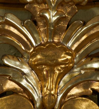 Zdjęcie nr 15: Obraz w kształcie pionowego prostokąta, z przedstawieniem Matki Boskiej z Dzieciątkiem, na niebieskim tle dekorowanym srebrzoną kratką, z malowanymi na drewnie partiami twarzy, dłoni i stóp oraz partiami szat i insygniami zasłoniętymi przez sukienki. Matka Boska ukazana w półpostaci, zwrócona delikatnie w trzech czwartych w lewą stronę, na lewym przedramieniu podtrzymuje Dzieciątko, a w prawej dłoni trzyma berło. Twarz pociągła, owalna, o dużych oczach, prostym, długim nosie i pełnych ustach, z odsłoniętym dużym prawym uchem. Łagodne rysy wydobyte zostały ostrym kontrastem światłocienia. Na głowie ma koronę zamkniętą, wokół głowy glorię promienistą i nimb zamknięty. Ubrana jest w suknię, dekorowaną gałązkami kwiatowymi, przepasaną w talii wstążką oraz płaszcz narzucony na ramiona, z ośmioramienną gwiazdą na prawym ramieniu, dekorowany ornamentem rocaille&#039;owym z ośmioramienną gwiazdą na prawym ramieniu. Dzieciątko w pozycji siedzącej, zwrócone jest w trzech czwartych w prawą stronę, prawą dłonią błogosławi, lewą przytrzymuje na kolanie jabłko królewskie. Jego twarz jest okrągła o rysach wydobytych silnym światłocieniem, o dużych oczach, niewielkim nosie i pełnych ustach z odsłoniętym lewym, dużym uchem. Na głowie ma koronę zamkniętą, wokół twarzy glorię promienistą oraz nimb zamknięty. Ubrane jest w tunikę dekorowaną gałązkami kwiatowymi i lamówką. Obraz ujęty posrebrzaną ramą z plastycznym, rokokowym i pozłacanym ornamentem. 