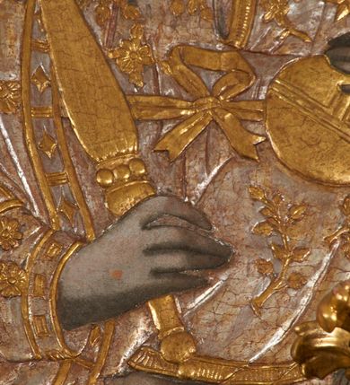 Zdjęcie nr 21: Obraz w kształcie pionowego prostokąta, z przedstawieniem Matki Boskiej z Dzieciątkiem, na niebieskim tle dekorowanym srebrzoną kratką, z malowanymi na drewnie partiami twarzy, dłoni i stóp oraz partiami szat i insygniami zasłoniętymi przez sukienki. Matka Boska ukazana w półpostaci, zwrócona delikatnie w trzech czwartych w lewą stronę, na lewym przedramieniu podtrzymuje Dzieciątko, a w prawej dłoni trzyma berło. Twarz pociągła, owalna, o dużych oczach, prostym, długim nosie i pełnych ustach, z odsłoniętym dużym prawym uchem. Łagodne rysy wydobyte zostały ostrym kontrastem światłocienia. Na głowie ma koronę zamkniętą, wokół głowy glorię promienistą i nimb zamknięty. Ubrana jest w suknię, dekorowaną gałązkami kwiatowymi, przepasaną w talii wstążką oraz płaszcz narzucony na ramiona, z ośmioramienną gwiazdą na prawym ramieniu, dekorowany ornamentem rocaille'owym z ośmioramienną gwiazdą na prawym ramieniu. Dzieciątko w pozycji siedzącej, zwrócone jest w trzech czwartych w prawą stronę, prawą dłonią błogosławi, lewą przytrzymuje na kolanie jabłko królewskie. Jego twarz jest okrągła o rysach wydobytych silnym światłocieniem, o dużych oczach, niewielkim nosie i pełnych ustach z odsłoniętym lewym, dużym uchem. Na głowie ma koronę zamkniętą, wokół twarzy glorię promienistą oraz nimb zamknięty. Ubrane jest w tunikę dekorowaną gałązkami kwiatowymi i lamówką. Obraz ujęty posrebrzaną ramą z plastycznym, rokokowym i pozłacanym ornamentem. 