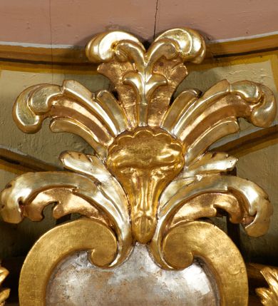 Zdjęcie nr 16: Obraz w kształcie pionowego prostokąta, z przedstawieniem Matki Boskiej z Dzieciątkiem, na niebieskim tle dekorowanym srebrzoną kratką, z malowanymi na drewnie partiami twarzy, dłoni i stóp oraz partiami szat i insygniami zasłoniętymi przez sukienki. Matka Boska ukazana w półpostaci, zwrócona delikatnie w trzech czwartych w lewą stronę, na lewym przedramieniu podtrzymuje Dzieciątko, a w prawej dłoni trzyma berło. Twarz pociągła, owalna, o dużych oczach, prostym, długim nosie i pełnych ustach, z odsłoniętym dużym prawym uchem. Łagodne rysy wydobyte zostały ostrym kontrastem światłocienia. Na głowie ma koronę zamkniętą, wokół głowy glorię promienistą i nimb zamknięty. Ubrana jest w suknię, dekorowaną gałązkami kwiatowymi, przepasaną w talii wstążką oraz płaszcz narzucony na ramiona, z ośmioramienną gwiazdą na prawym ramieniu, dekorowany ornamentem rocaille&#039;owym z ośmioramienną gwiazdą na prawym ramieniu. Dzieciątko w pozycji siedzącej, zwrócone jest w trzech czwartych w prawą stronę, prawą dłonią błogosławi, lewą przytrzymuje na kolanie jabłko królewskie. Jego twarz jest okrągła o rysach wydobytych silnym światłocieniem, o dużych oczach, niewielkim nosie i pełnych ustach z odsłoniętym lewym, dużym uchem. Na głowie ma koronę zamkniętą, wokół twarzy glorię promienistą oraz nimb zamknięty. Ubrane jest w tunikę dekorowaną gałązkami kwiatowymi i lamówką. Obraz ujęty posrebrzaną ramą z plastycznym, rokokowym i pozłacanym ornamentem. 