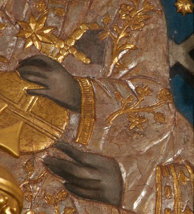 Zdjęcie nr 20: Obraz w kształcie pionowego prostokąta, z przedstawieniem Matki Boskiej z Dzieciątkiem, na niebieskim tle dekorowanym srebrzoną kratką, z malowanymi na drewnie partiami twarzy, dłoni i stóp oraz partiami szat i insygniami zasłoniętymi przez sukienki. Matka Boska ukazana w półpostaci, zwrócona delikatnie w trzech czwartych w lewą stronę, na lewym przedramieniu podtrzymuje Dzieciątko, a w prawej dłoni trzyma berło. Twarz pociągła, owalna, o dużych oczach, prostym, długim nosie i pełnych ustach, z odsłoniętym dużym prawym uchem. Łagodne rysy wydobyte zostały ostrym kontrastem światłocienia. Na głowie ma koronę zamkniętą, wokół głowy glorię promienistą i nimb zamknięty. Ubrana jest w suknię, dekorowaną gałązkami kwiatowymi, przepasaną w talii wstążką oraz płaszcz narzucony na ramiona, z ośmioramienną gwiazdą na prawym ramieniu, dekorowany ornamentem rocaille'owym z ośmioramienną gwiazdą na prawym ramieniu. Dzieciątko w pozycji siedzącej, zwrócone jest w trzech czwartych w prawą stronę, prawą dłonią błogosławi, lewą przytrzymuje na kolanie jabłko królewskie. Jego twarz jest okrągła o rysach wydobytych silnym światłocieniem, o dużych oczach, niewielkim nosie i pełnych ustach z odsłoniętym lewym, dużym uchem. Na głowie ma koronę zamkniętą, wokół twarzy glorię promienistą oraz nimb zamknięty. Ubrane jest w tunikę dekorowaną gałązkami kwiatowymi i lamówką. Obraz ujęty posrebrzaną ramą z plastycznym, rokokowym i pozłacanym ornamentem. 