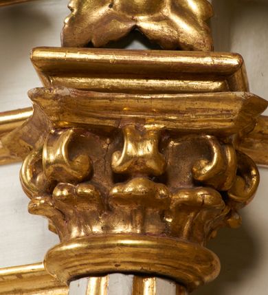 Zdjęcie nr 11: Tabernakulum architektoniczne, jednokondygnacyjne, pięcioosiowe. Osie wydzielone są sześcioma kanelowanymi kolumienkami na wysokich, profilowanych cokołach, z liściastymi kapitelami, podtrzymującymi profilowane belkowanie wyłamane na ich osiach. W polach pomiędzy kolumnami znajdują się nisze ujęte profilowaną ramą z uszakami. W czterech bocznych niszach, na trójdzielnych, profilowanych wspornikach stoją płaskorzeźbione postacie czterech ewangelistów na tle muszli palmetowych. Figurki są całopostaciowe, w ujęciu frontalnym, w złotych szatach, podtrzymują otwarte księgi, wskazując na tekst. Drzwiczki znajdują się na osi środkowej, zamknięte są półkoliście, płaskorzeźbione z przedstawieniem kielicha z koroną cierniową i z hostią w glorii promienistej. Kielich flankowany jest kłosami zbóż i winną latoroślą oraz winogronami. W partii belkowania płaskorzeźbiona dekoracja złożona z naprzemiennie ułożonych główek anielskich o złotych skrzydłach i płaskich rozetek. Tron wystawienia w formie baldachimu, z lambrekinem i chwostami, zwieńczony jest kulą z krzyżem, z podwieszonym z tyłu paludamentem podtrzymywanym przez parę puttów. Struktura polichromowana na biało, profile i detale pozłocone. 