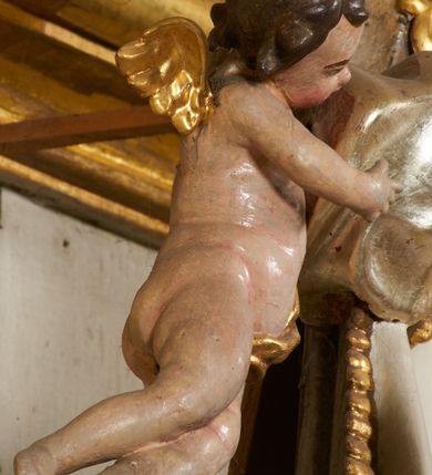 Zdjęcie nr 22: Tabernakulum architektoniczne, jednokondygnacyjne, pięcioosiowe. Osie wydzielone są sześcioma kanelowanymi kolumienkami na wysokich, profilowanych cokołach, z liściastymi kapitelami, podtrzymującymi profilowane belkowanie wyłamane na ich osiach. W polach pomiędzy kolumnami znajdują się nisze ujęte profilowaną ramą z uszakami. W czterech bocznych niszach, na trójdzielnych, profilowanych wspornikach stoją płaskorzeźbione postacie czterech ewangelistów na tle muszli palmetowych. Figurki są całopostaciowe, w ujęciu frontalnym, w złotych szatach, podtrzymują otwarte księgi, wskazując na tekst. Drzwiczki znajdują się na osi środkowej, zamknięte są półkoliście, płaskorzeźbione z przedstawieniem kielicha z koroną cierniową i z hostią w glorii promienistej. Kielich flankowany jest kłosami zbóż i winną latoroślą oraz winogronami. W partii belkowania płaskorzeźbiona dekoracja złożona z naprzemiennie ułożonych główek anielskich o złotych skrzydłach i płaskich rozetek. Tron wystawienia w formie baldachimu, z lambrekinem i chwostami, zwieńczony jest kulą z krzyżem, z podwieszonym z tyłu paludamentem podtrzymywanym przez parę puttów. Struktura polichromowana na biało, profile i detale pozłocone. 