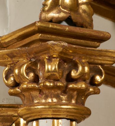 Zdjęcie nr 12: Tabernakulum architektoniczne, jednokondygnacyjne, pięcioosiowe. Osie wydzielone są sześcioma kanelowanymi kolumienkami na wysokich, profilowanych cokołach, z liściastymi kapitelami, podtrzymującymi profilowane belkowanie wyłamane na ich osiach. W polach pomiędzy kolumnami znajdują się nisze ujęte profilowaną ramą z uszakami. W czterech bocznych niszach, na trójdzielnych, profilowanych wspornikach stoją płaskorzeźbione postacie czterech ewangelistów na tle muszli palmetowych. Figurki są całopostaciowe, w ujęciu frontalnym, w złotych szatach, podtrzymują otwarte księgi, wskazując na tekst. Drzwiczki znajdują się na osi środkowej, zamknięte są półkoliście, płaskorzeźbione z przedstawieniem kielicha z koroną cierniową i z hostią w glorii promienistej. Kielich flankowany jest kłosami zbóż i winną latoroślą oraz winogronami. W partii belkowania płaskorzeźbiona dekoracja złożona z naprzemiennie ułożonych główek anielskich o złotych skrzydłach i płaskich rozetek. Tron wystawienia w formie baldachimu, z lambrekinem i chwostami, zwieńczony jest kulą z krzyżem, z podwieszonym z tyłu paludamentem podtrzymywanym przez parę puttów. Struktura polichromowana na biało, profile i detale pozłocone. 