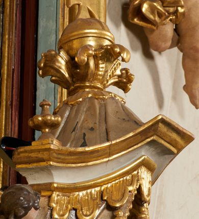 Zdjęcie nr 10: Tabernakulum architektoniczne, jednokondygnacyjne, pięcioosiowe. Osie wydzielone są sześcioma kanelowanymi kolumienkami na wysokich, profilowanych cokołach, z liściastymi kapitelami, podtrzymującymi profilowane belkowanie wyłamane na ich osiach. W polach pomiędzy kolumnami znajdują się nisze ujęte profilowaną ramą z uszakami. W czterech bocznych niszach, na trójdzielnych, profilowanych wspornikach stoją płaskorzeźbione postacie czterech ewangelistów na tle muszli palmetowych. Figurki są całopostaciowe, w ujęciu frontalnym, w złotych szatach, podtrzymują otwarte księgi, wskazując na tekst. Drzwiczki znajdują się na osi środkowej, zamknięte są półkoliście, płaskorzeźbione z przedstawieniem kielicha z koroną cierniową i z hostią w glorii promienistej. Kielich flankowany jest kłosami zbóż i winną latoroślą oraz winogronami. W partii belkowania płaskorzeźbiona dekoracja złożona z naprzemiennie ułożonych główek anielskich o złotych skrzydłach i płaskich rozetek. Tron wystawienia w formie baldachimu, z lambrekinem i chwostami, zwieńczony jest kulą z krzyżem, z podwieszonym z tyłu paludamentem podtrzymywanym przez parę puttów. Struktura polichromowana na biało, profile i detale pozłocone. 