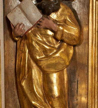 Zdjęcie nr 18: Tabernakulum architektoniczne, jednokondygnacyjne, pięcioosiowe. Osie wydzielone są sześcioma kanelowanymi kolumienkami na wysokich, profilowanych cokołach, z liściastymi kapitelami, podtrzymującymi profilowane belkowanie wyłamane na ich osiach. W polach pomiędzy kolumnami znajdują się nisze ujęte profilowaną ramą z uszakami. W czterech bocznych niszach, na trójdzielnych, profilowanych wspornikach stoją płaskorzeźbione postacie czterech ewangelistów na tle muszli palmetowych. Figurki są całopostaciowe, w ujęciu frontalnym, w złotych szatach, podtrzymują otwarte księgi, wskazując na tekst. Drzwiczki znajdują się na osi środkowej, zamknięte są półkoliście, płaskorzeźbione z przedstawieniem kielicha z koroną cierniową i z hostią w glorii promienistej. Kielich flankowany jest kłosami zbóż i winną latoroślą oraz winogronami. W partii belkowania płaskorzeźbiona dekoracja złożona z naprzemiennie ułożonych główek anielskich o złotych skrzydłach i płaskich rozetek. Tron wystawienia w formie baldachimu, z lambrekinem i chwostami, zwieńczony jest kulą z krzyżem, z podwieszonym z tyłu paludamentem podtrzymywanym przez parę puttów. Struktura polichromowana na biało, profile i detale pozłocone. 